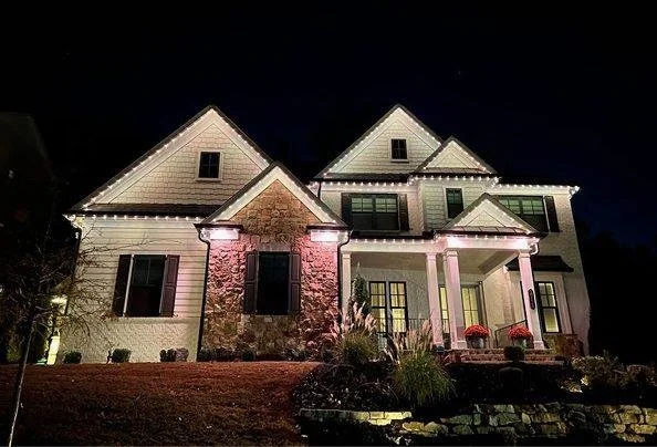 A large, two-story house decorated with Christmas lights at night.