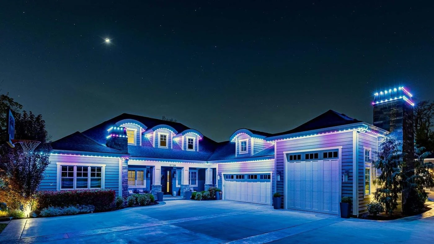 A house decorated with colorful Christmas lights at night, with a clear sky and visible stars, and a crescent moon above.