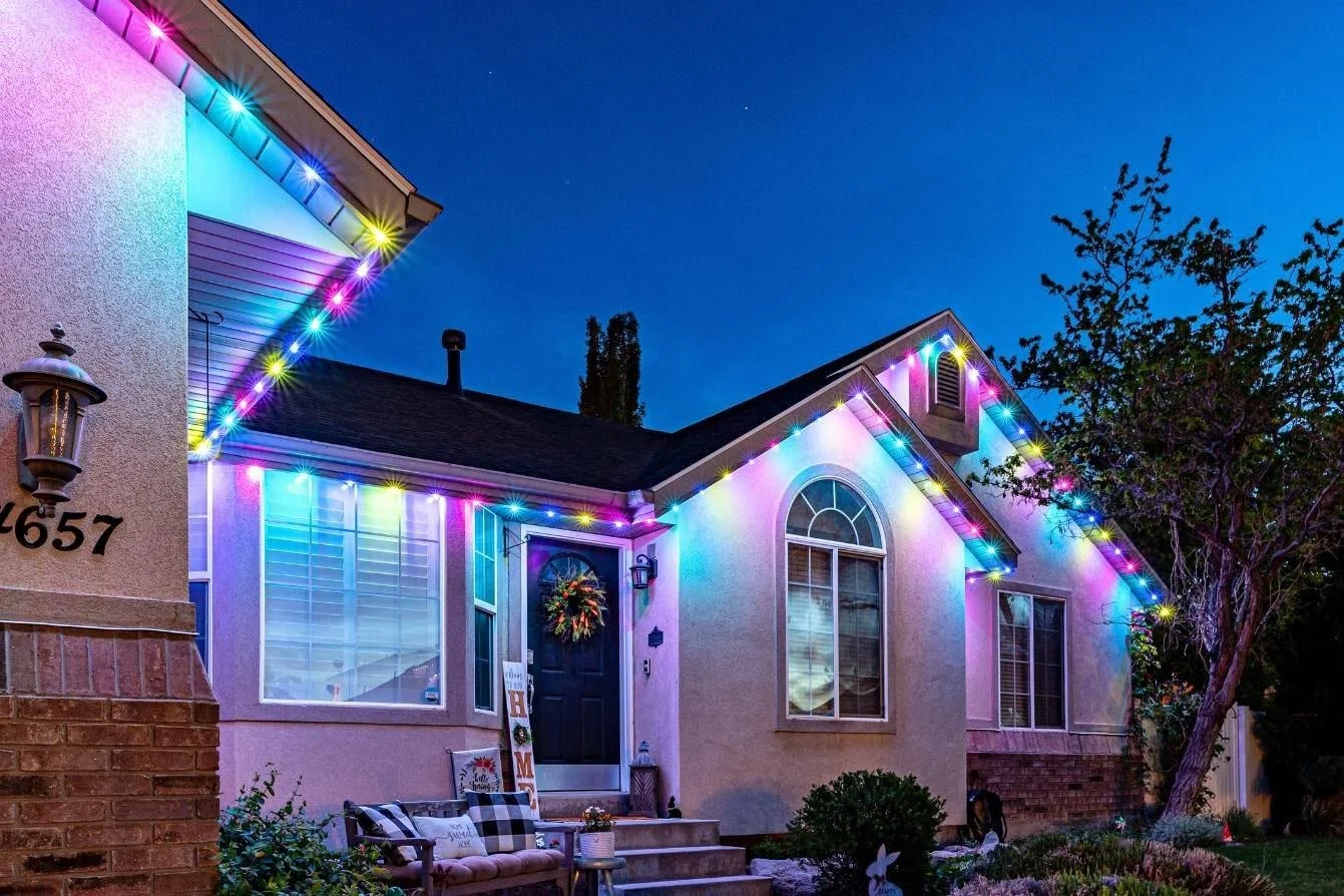 House decorated with colorful Christmas lights at night, with a decorated front door and outdoor furniture