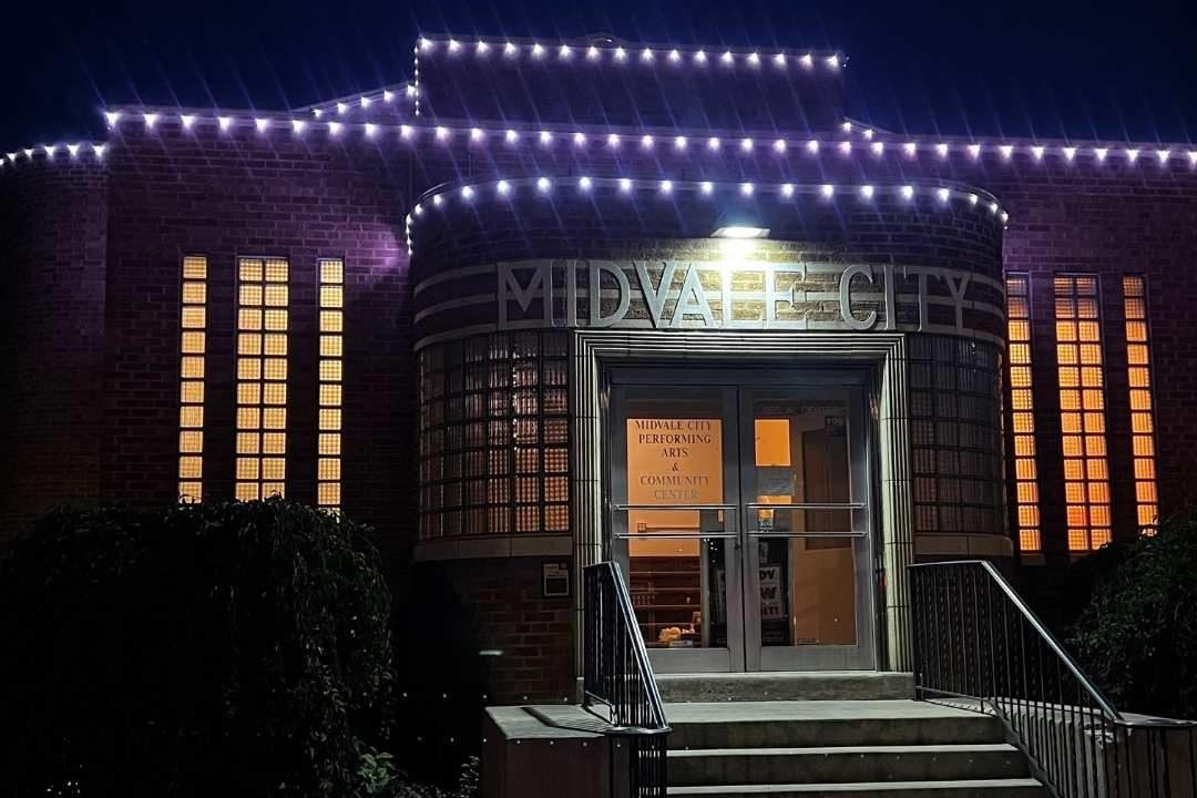 Nighttime exterior view of Midvale City Performing Arts and Community Center with illuminated string lights and glowing windows.
