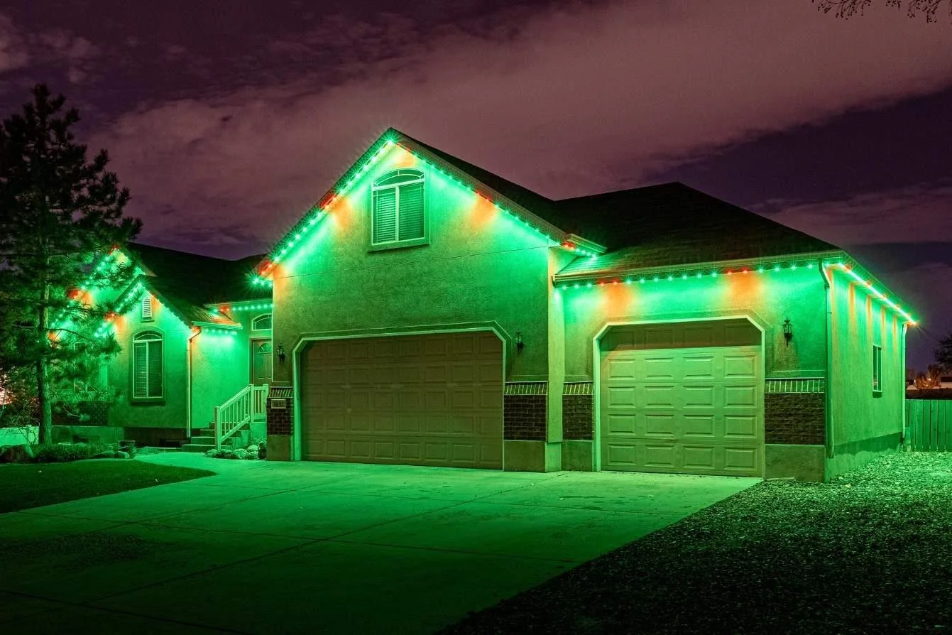 A house at night decorated with green Christmas lights along the roofline and around the garage doors.