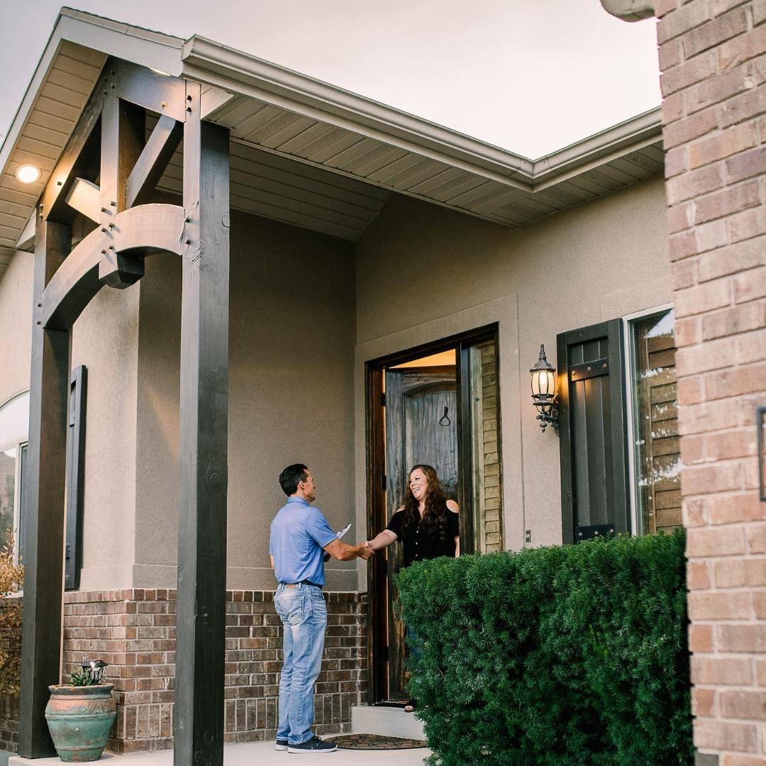 A man and a woman shaking hands at the front door of a house while smiling.