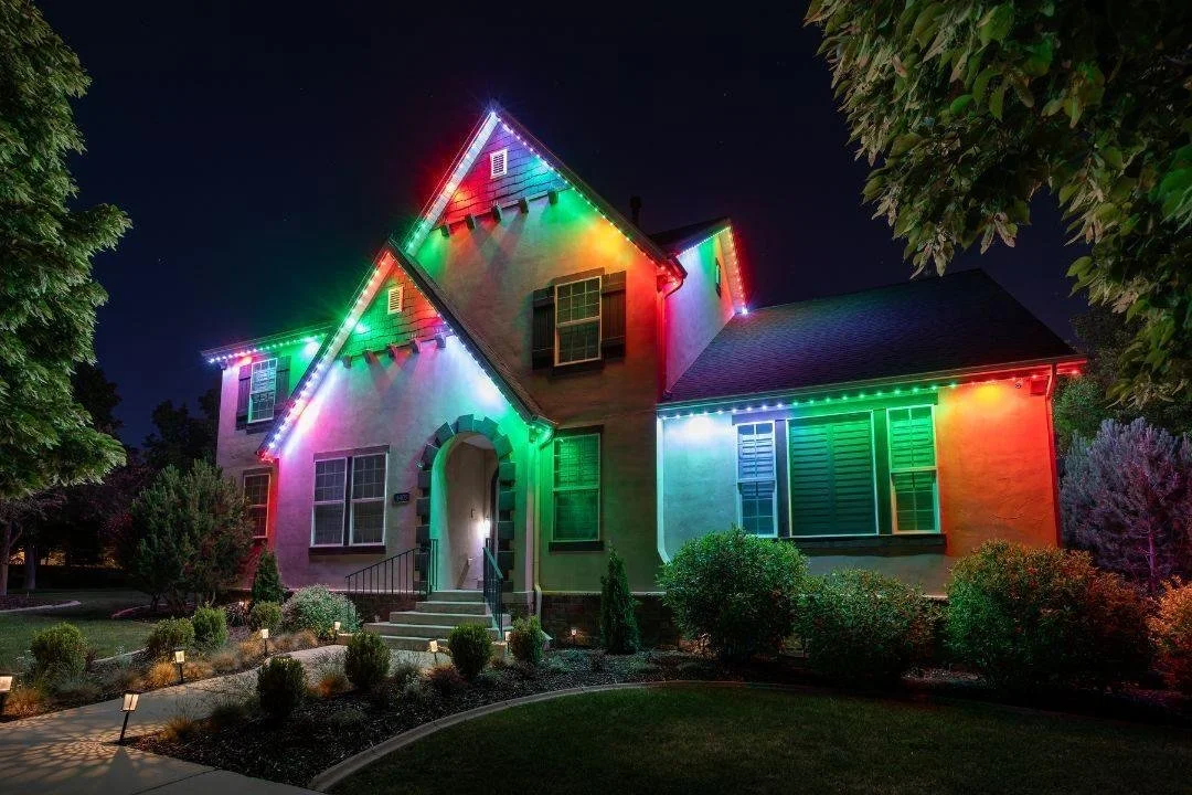 A house decorated with colorful Christmas lights at night, illuminating the front facade and roof.