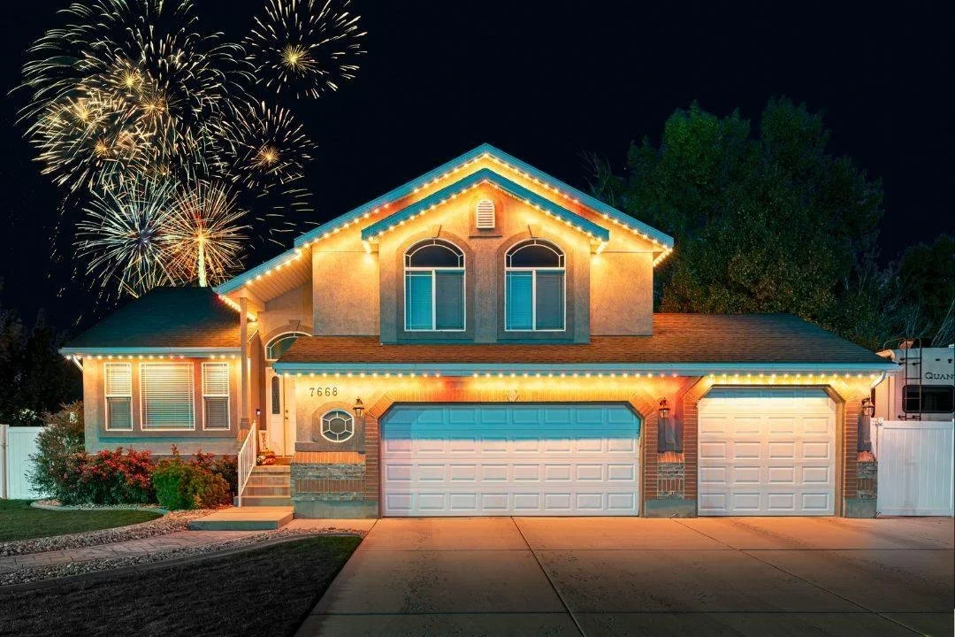 A two-story house decorated with colorful holiday lights at night, with fireworks in the sky above.