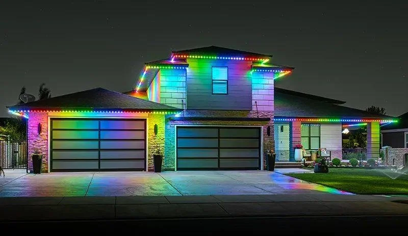 A house decorated with colorful Christmas lights at night, highlighting the roof, windows, and driveway.