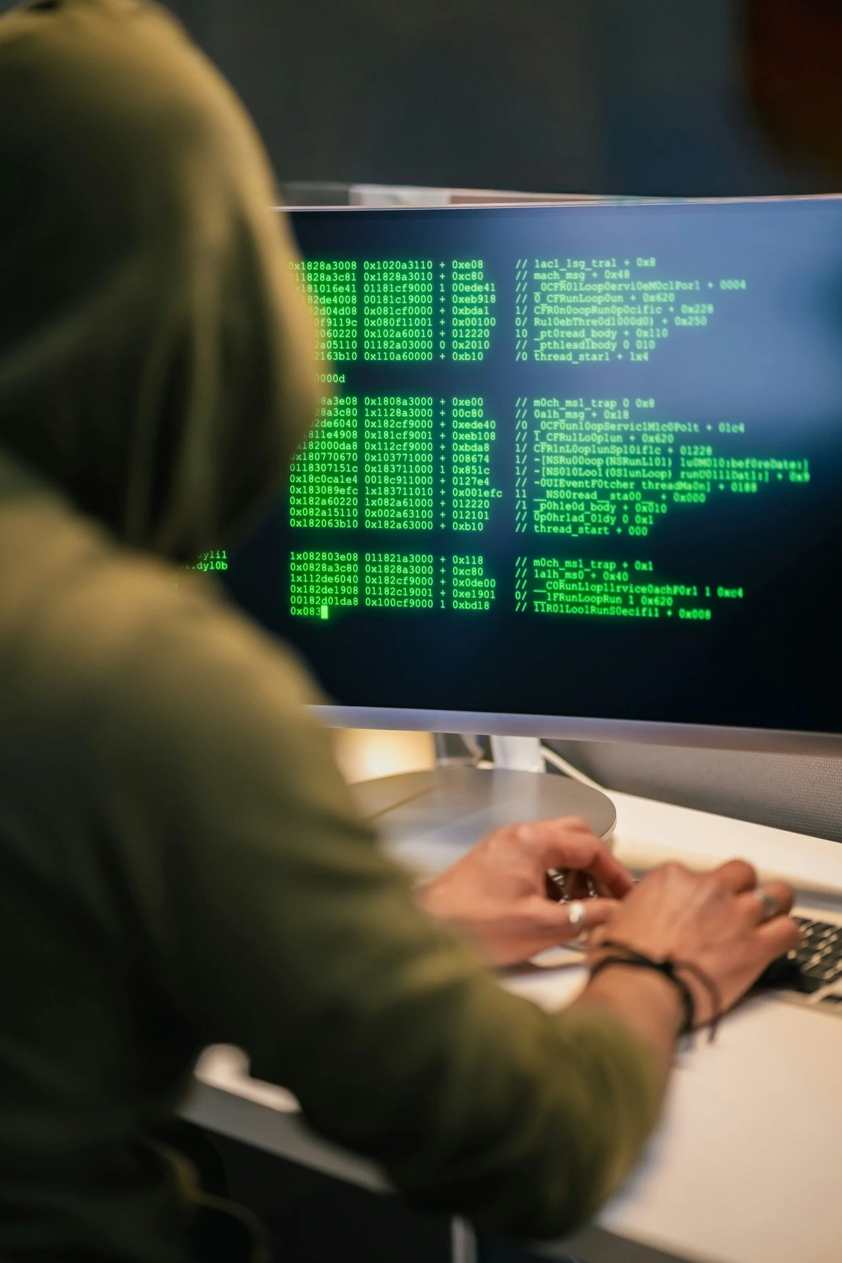 Close-up of a computer monitor displaying green code, with hands typing on a keyboard in the foreground, in an office setting stealing the identity of the victim.