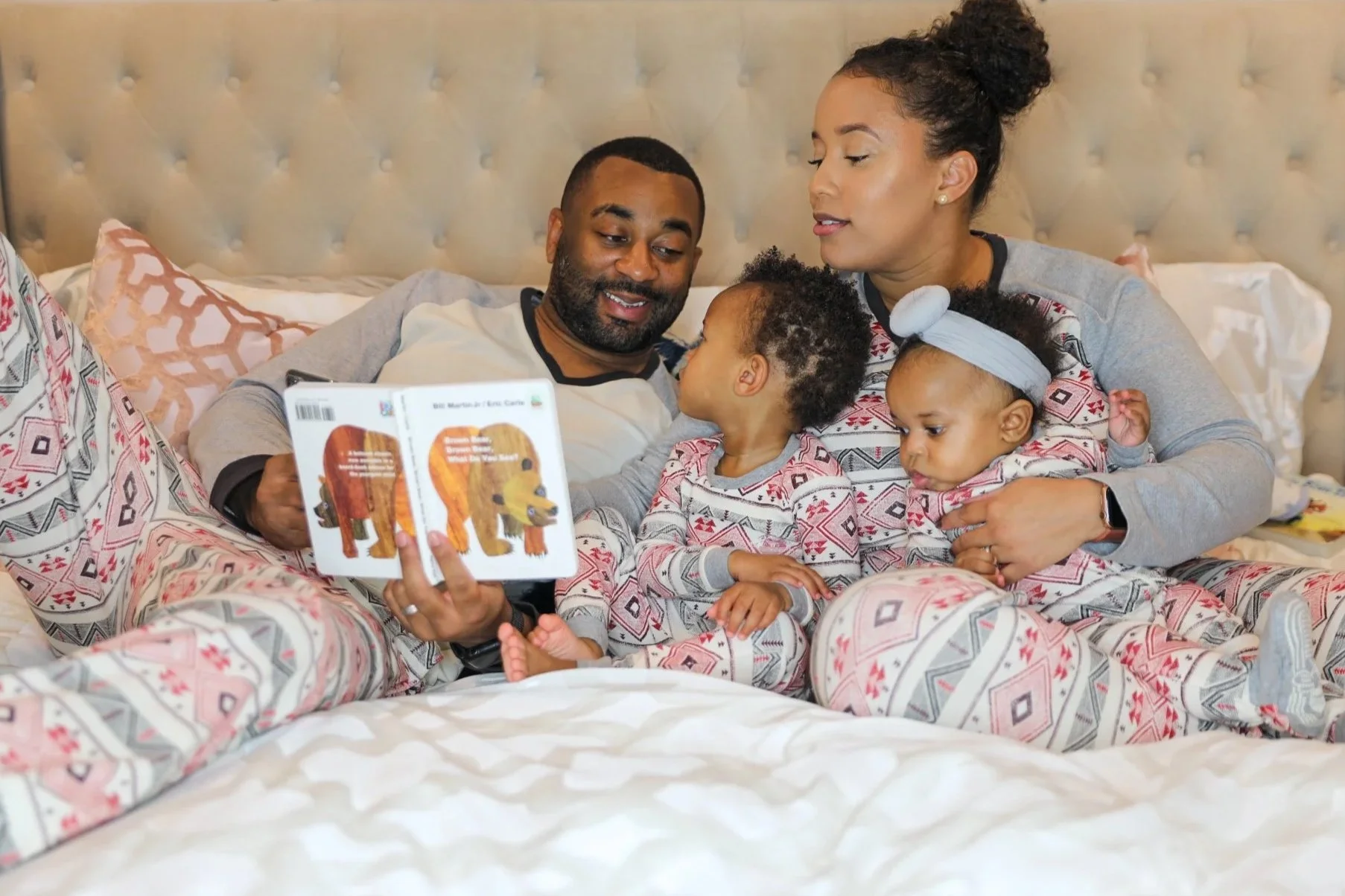 A family of four sitting on a bed, reading a children's book about animals while wearing matching pajamas with geometric and animal patterns.