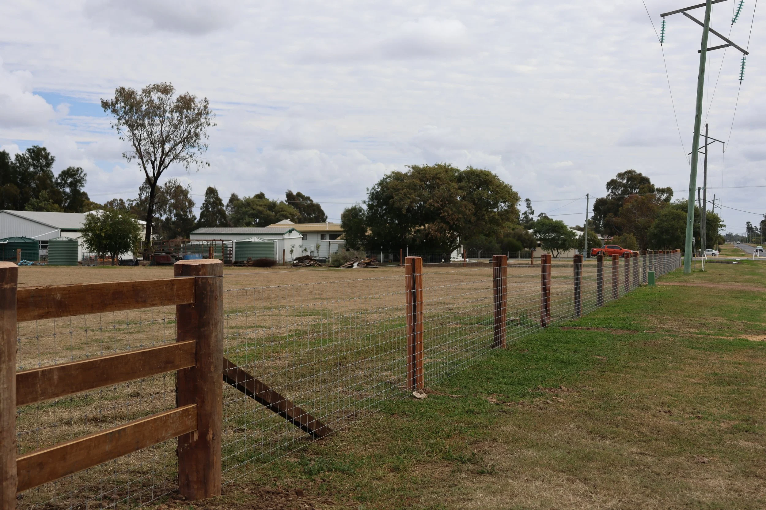 A rural scene with a wooden and wire fence in the foreground