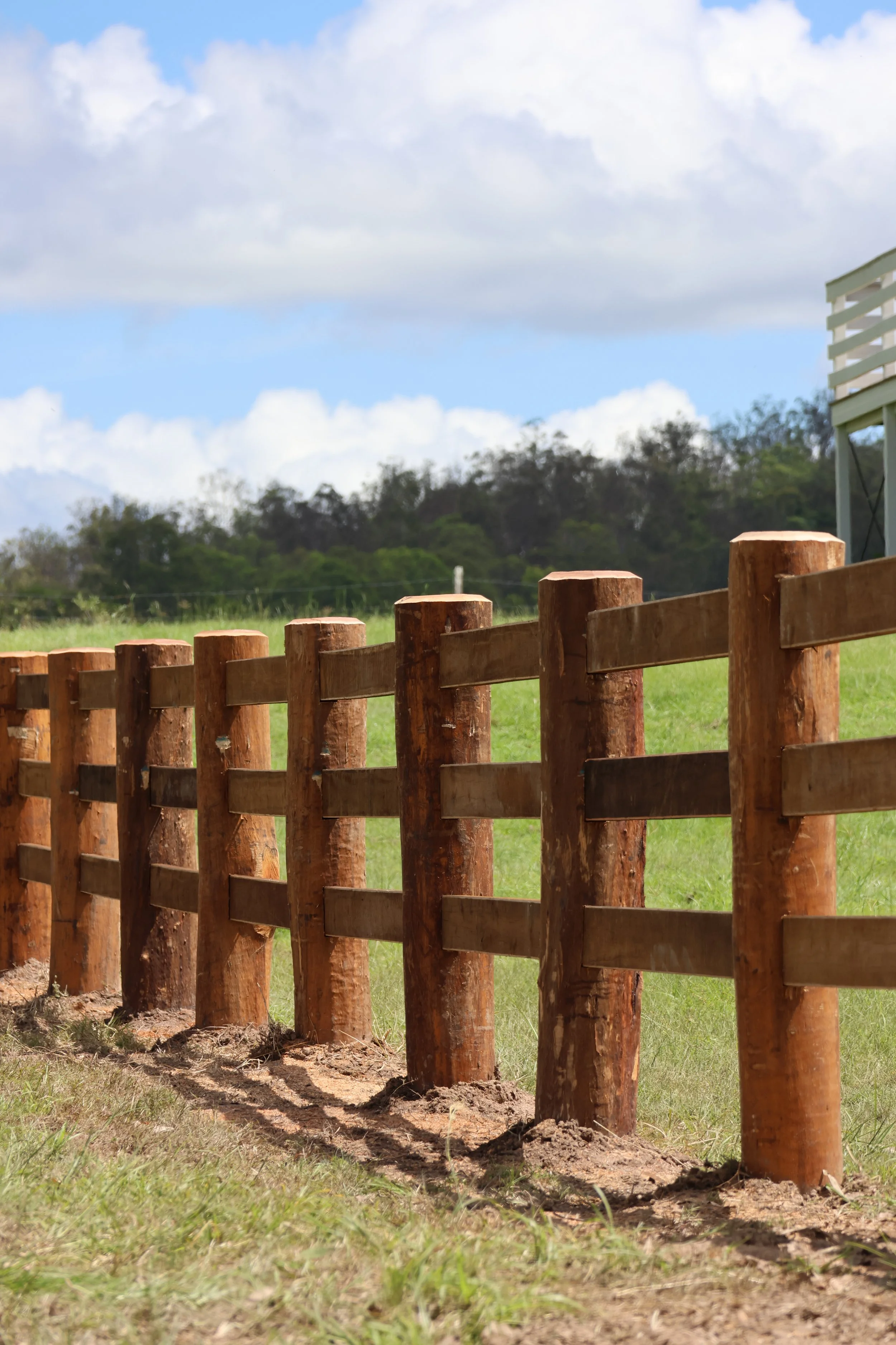 A wooden fence with vertical posts and horizontal rails is being installed in a grassy yard.