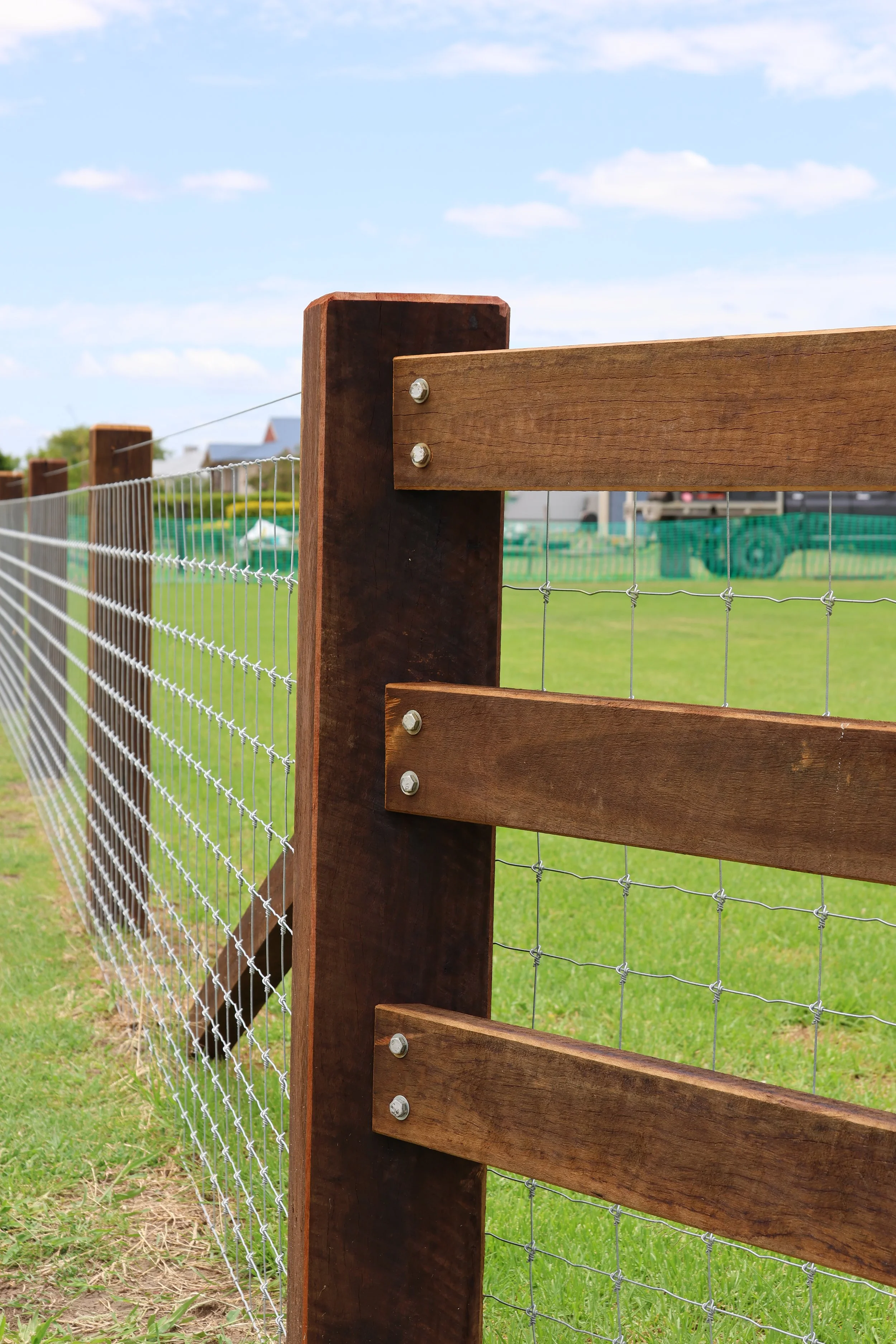 Close-up of a wooden fence post with metal bolts, with a wire mesh fence 