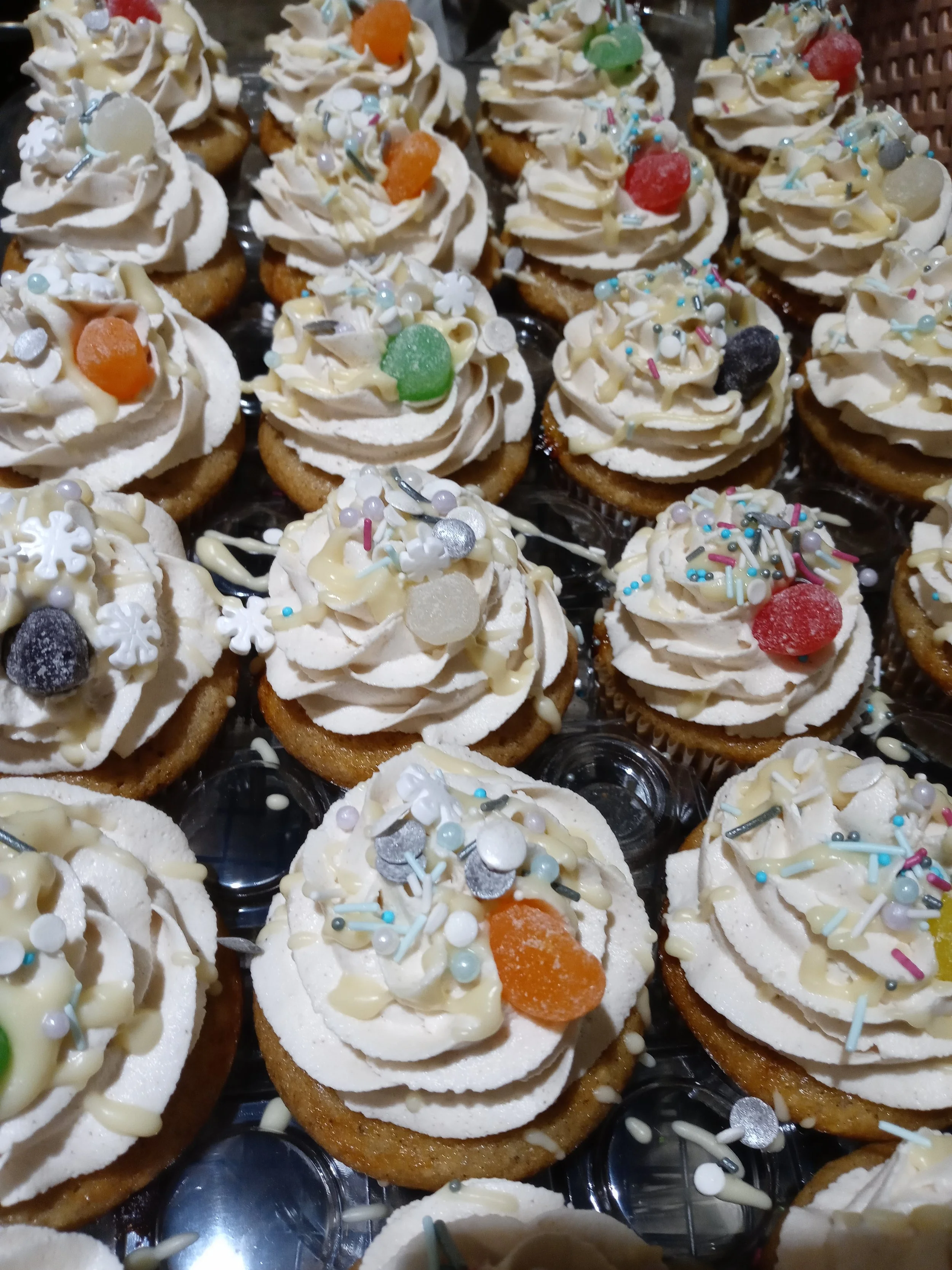 SweetSpiracy Sugarplum cupcakes topped with white frosting, colorful sprinkles, and assorted candy.