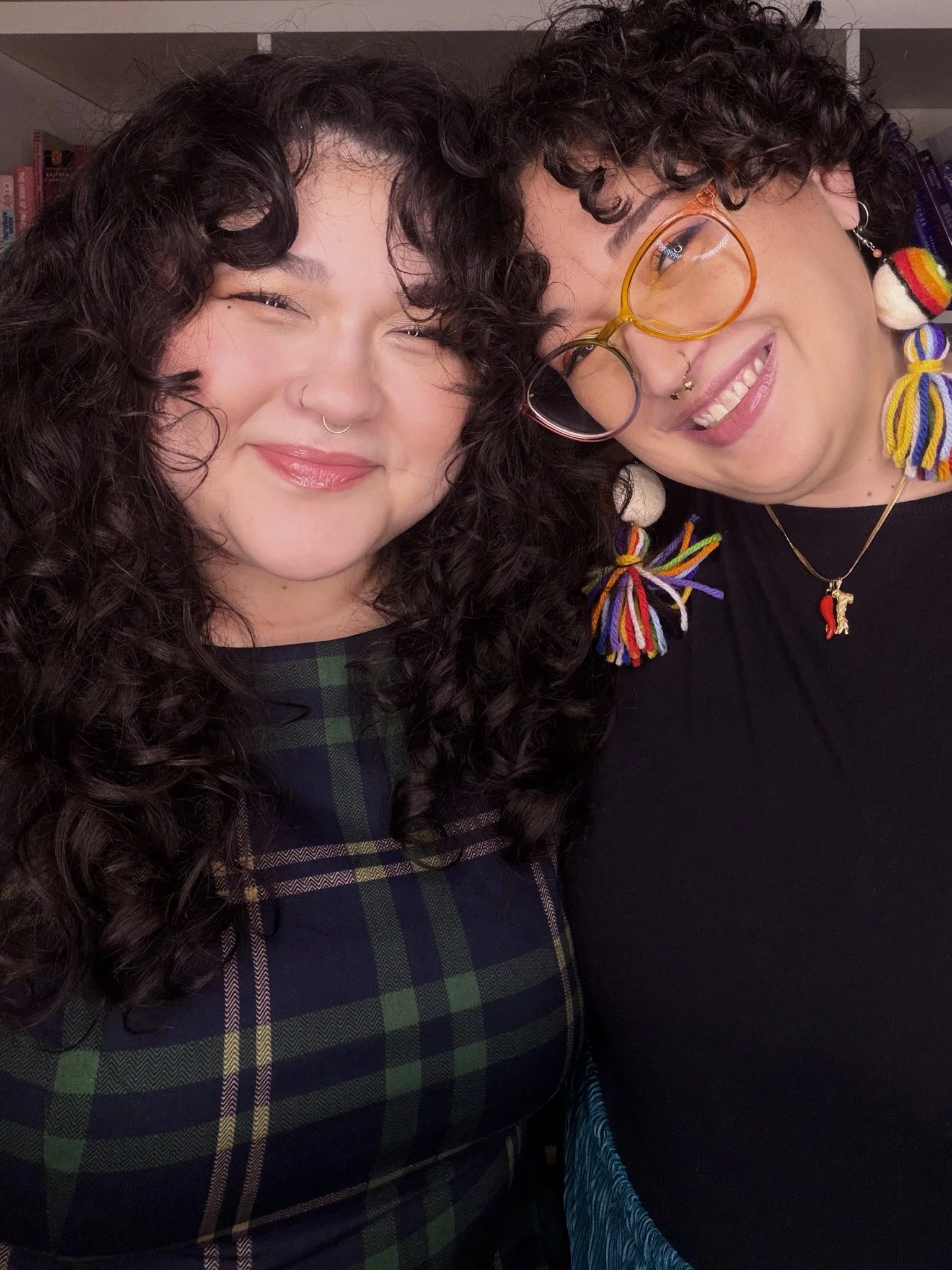 Two people with curly hair smile at the camera, with their heads leaning against each other.