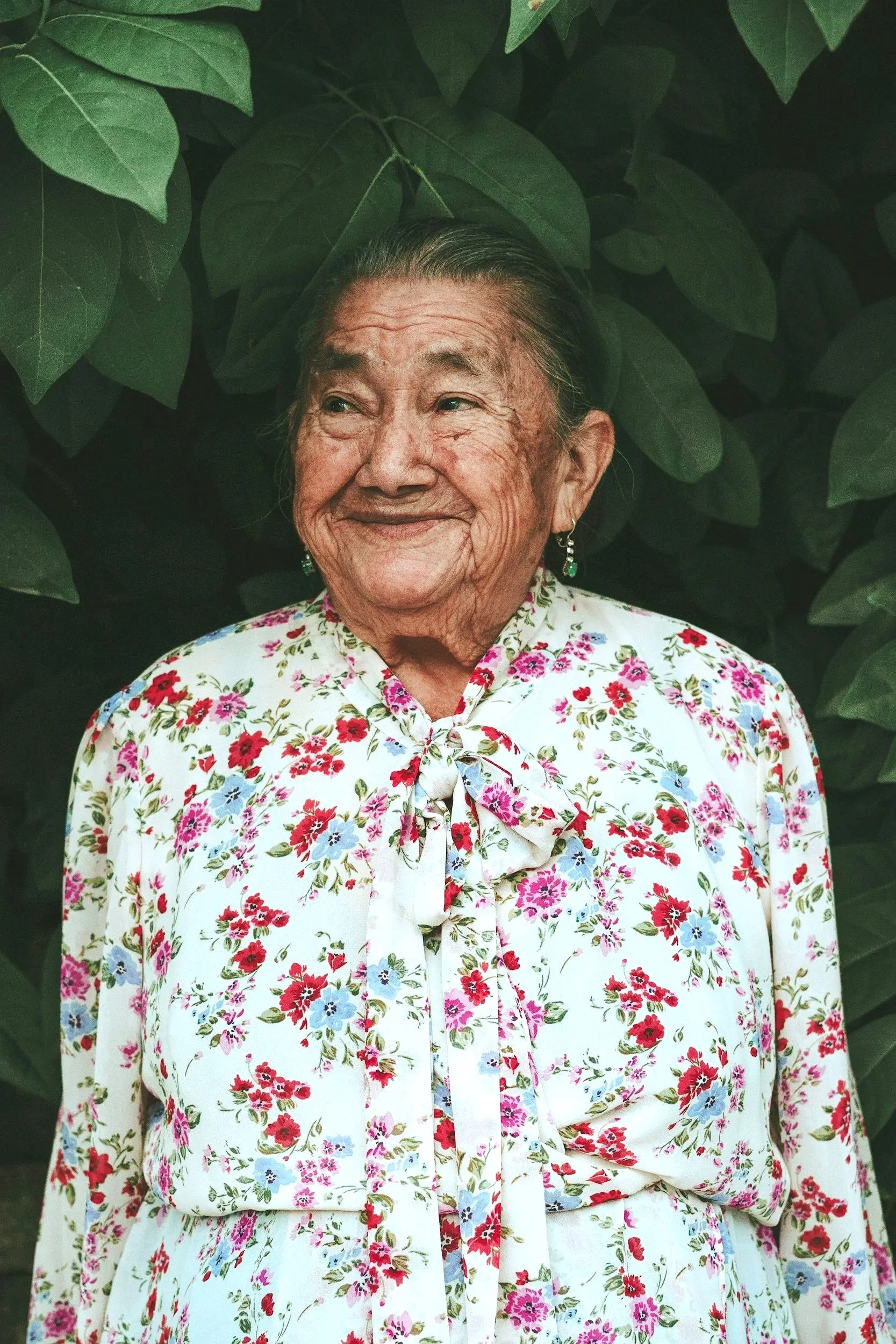 An elder or senior citizen smiling looking off camera wearing a floral shirt surrounded by leaves.