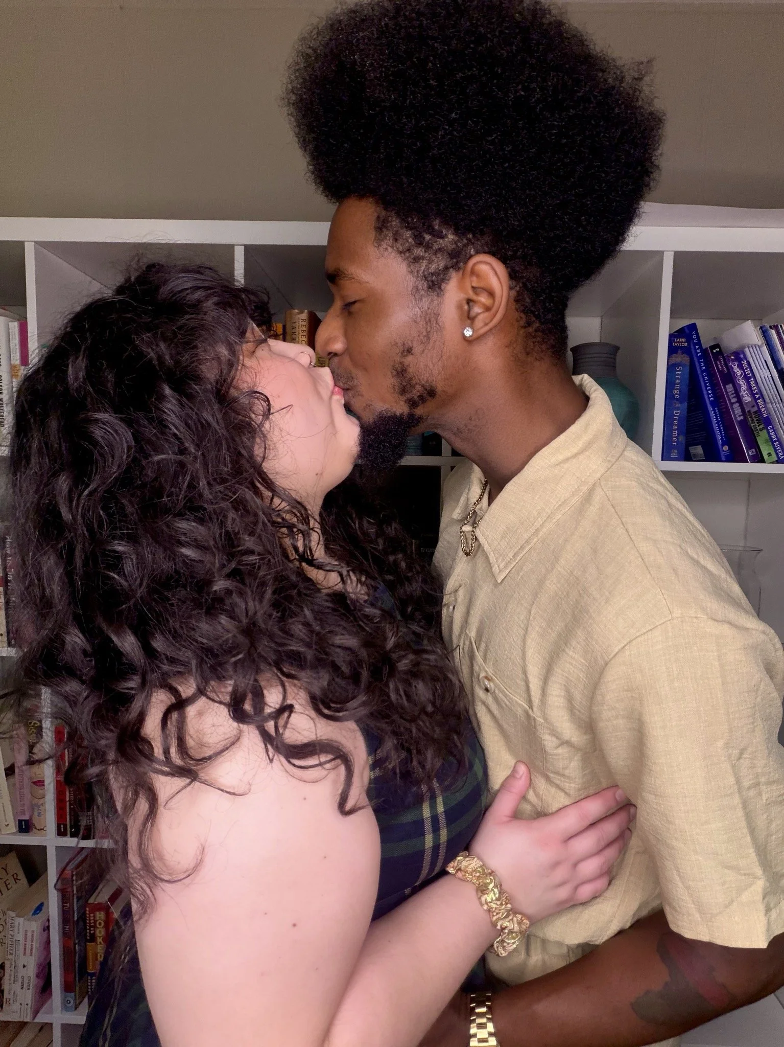Two people kissing, one with long wavy hair and the other with an afro face towards each other, side profiles to the camera.