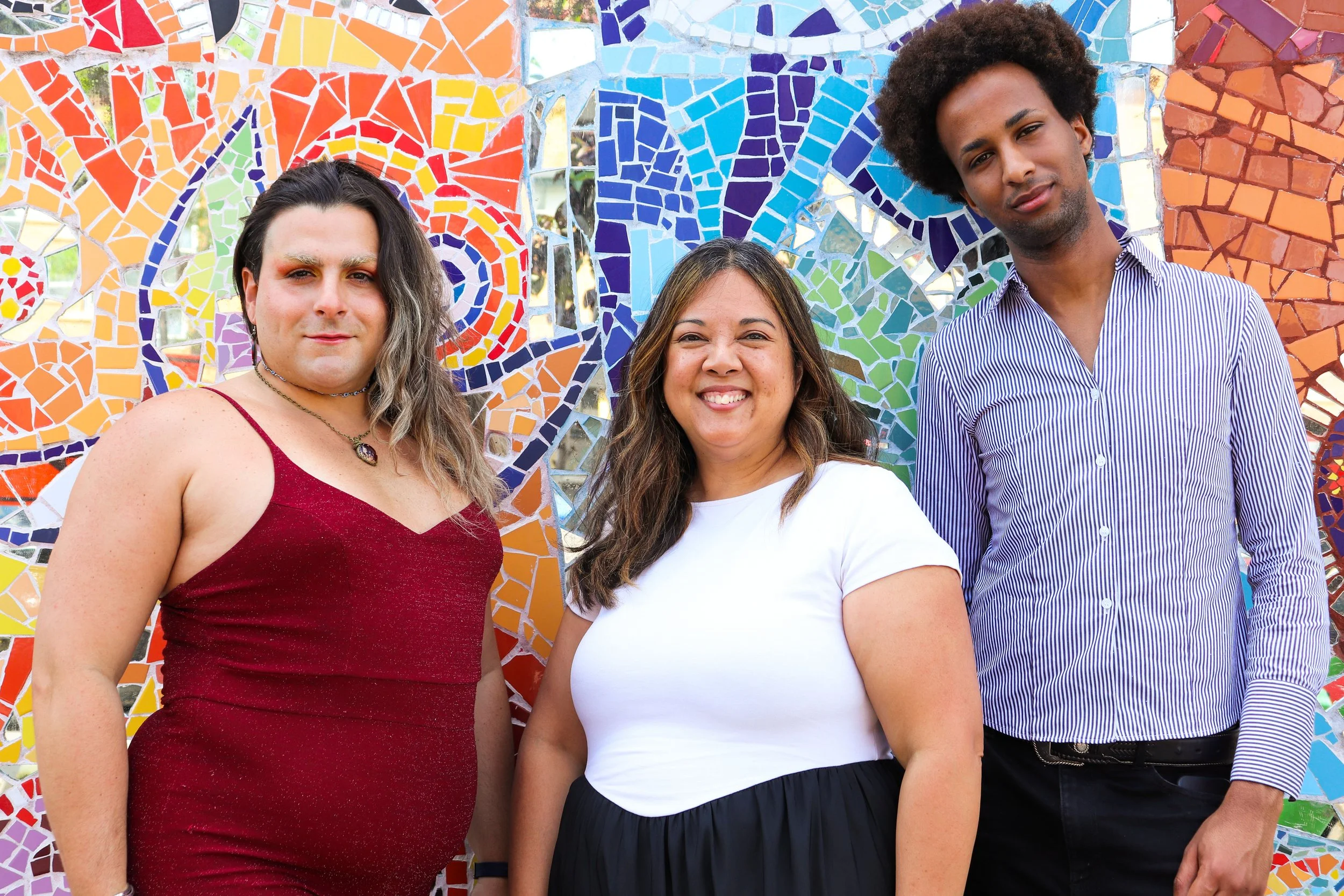 Colorful group portrait of three people standing in front of a mural of colorful glass and mirrors.