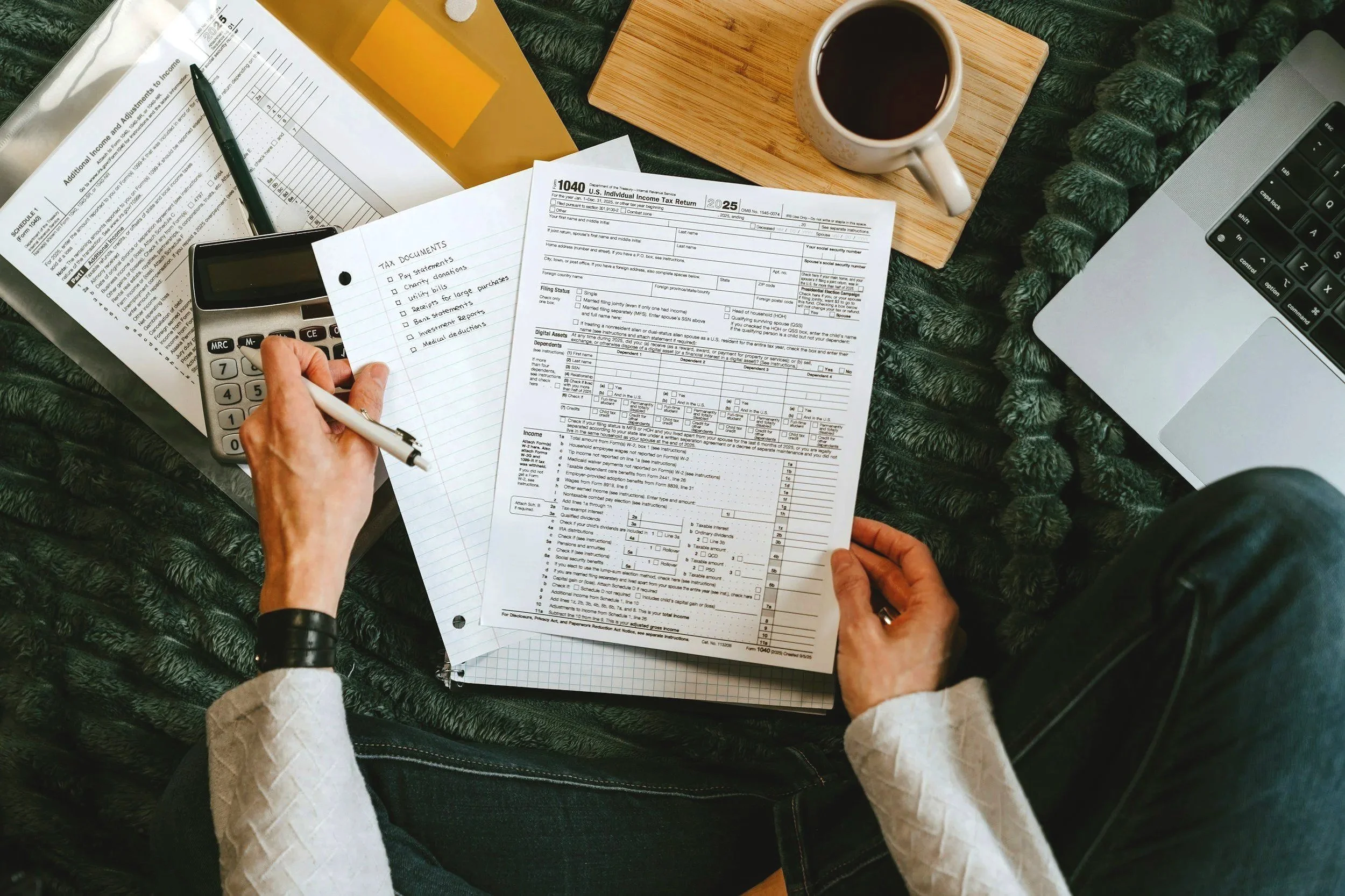 Two hands, perspective of a person looking down at a tax document with coffee on the table and a pen in hand.