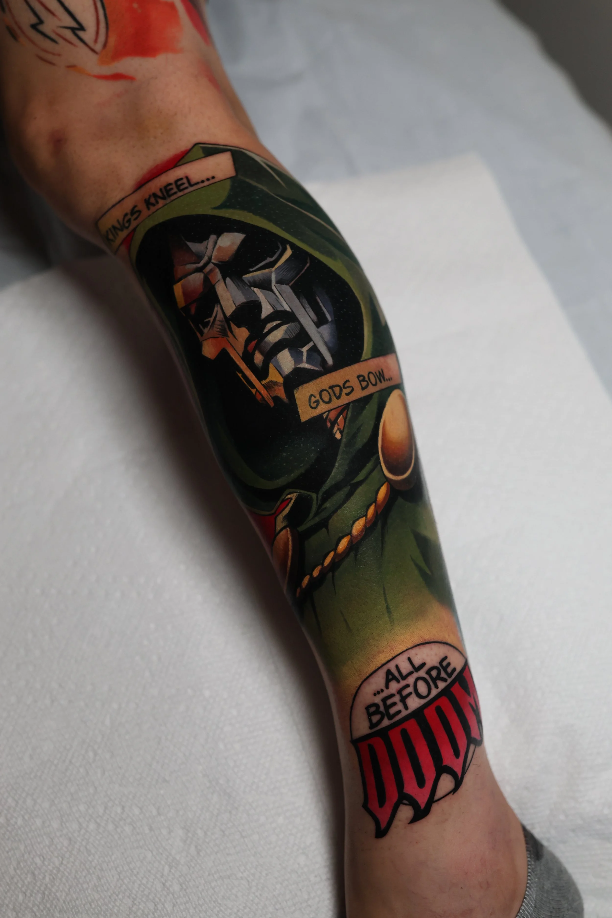 a colorful tattoo of the character Dr. Doom from Marvel with text that says "kings kneel...gods bow...all before DOOM"