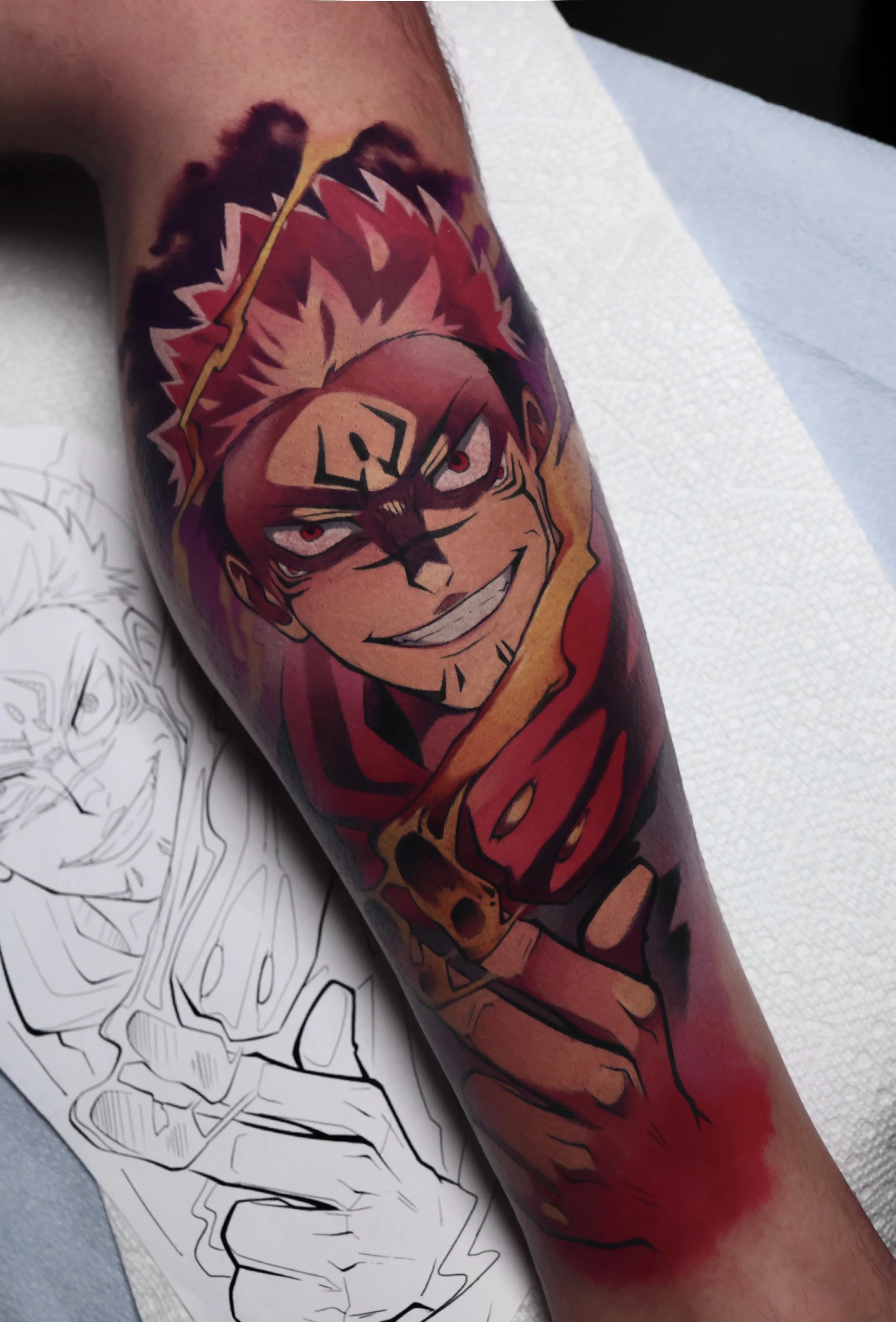 colorful tattoo of Sakuna from Jujutsu Kaisen grinning and using a fiery technique with his hands.