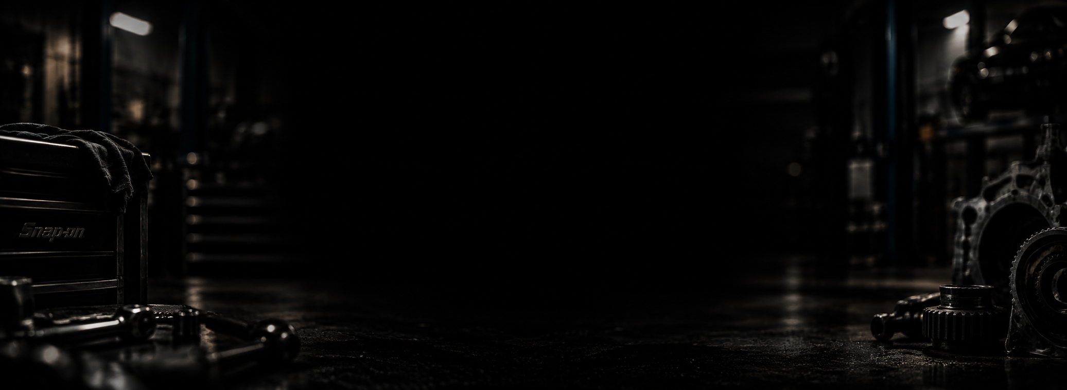 A dark, industrial workshop with automotive parts and tools scattered on the floor and shelves in the background.