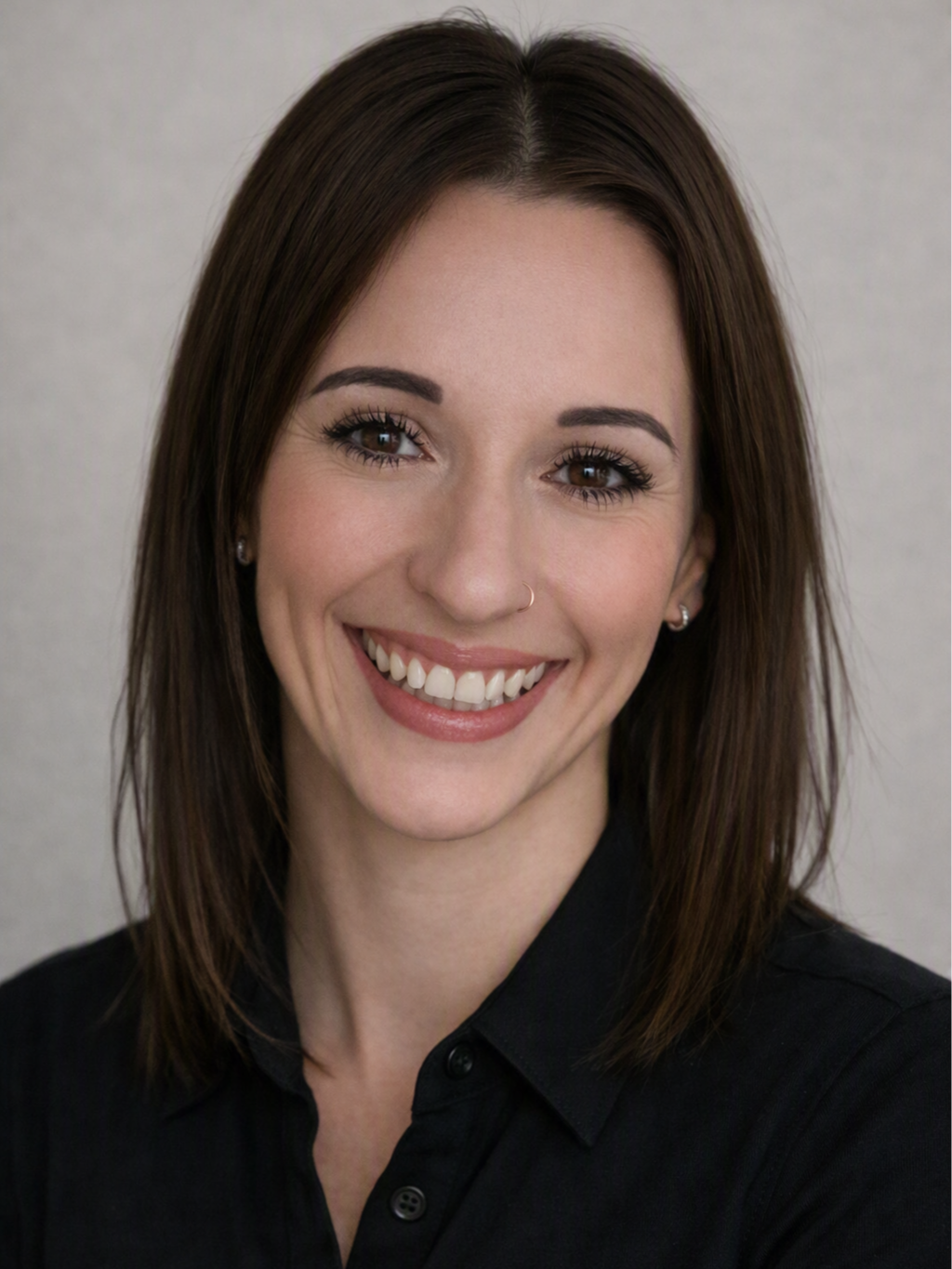 Close-up portrait of a smiling woman with brown hair, wearing a black button-up shirt and small earrings.
