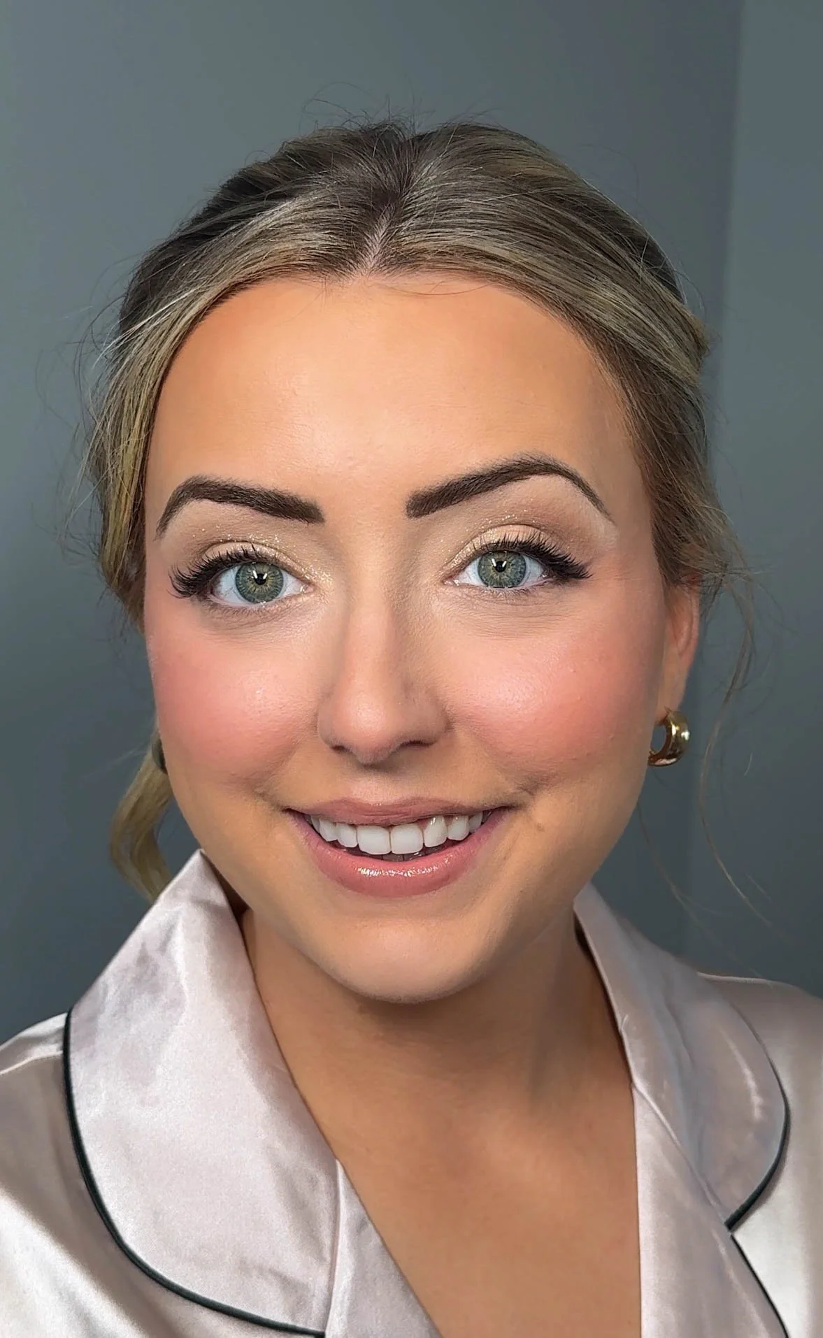Soft bridal makeup with glowing skin, rosy cheeks and defined blue eyes.