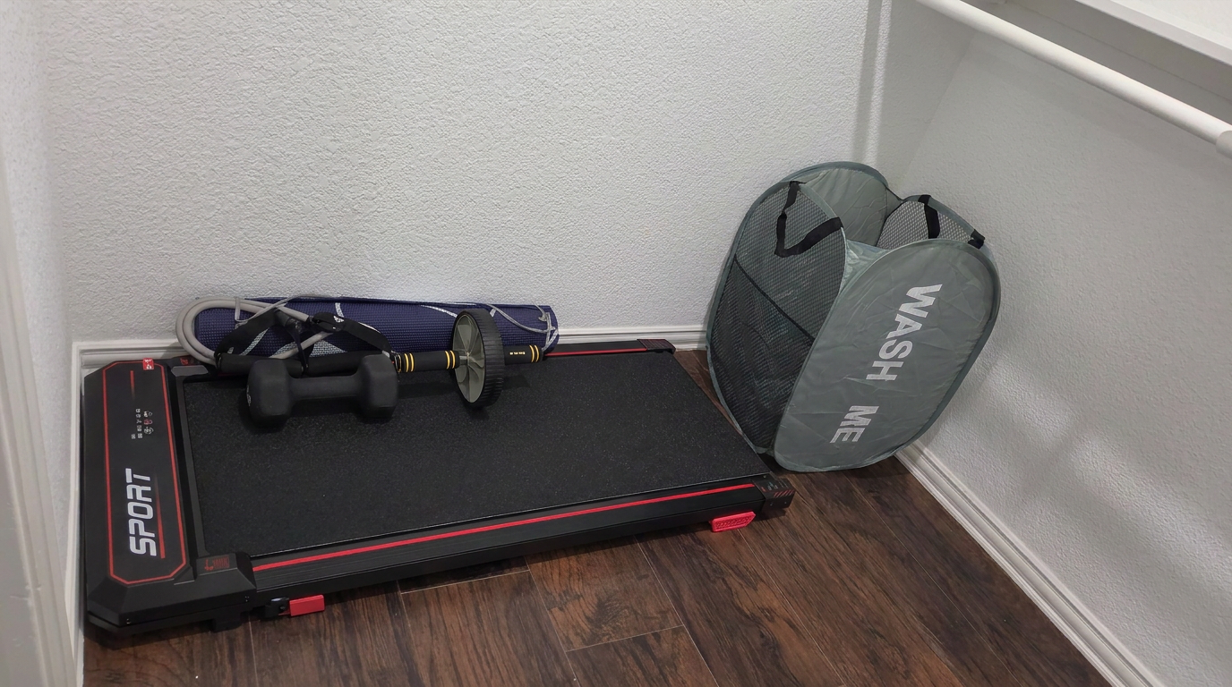Home workout corner with compact treadmill, dumbbells, jump rope, and a washable laundry hamper on wooden flooring.