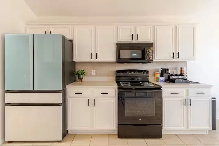 Kitchen with white cabinets, black refrigerator, stove, microwave, and countertop with small kitchen tools and a potted plant.