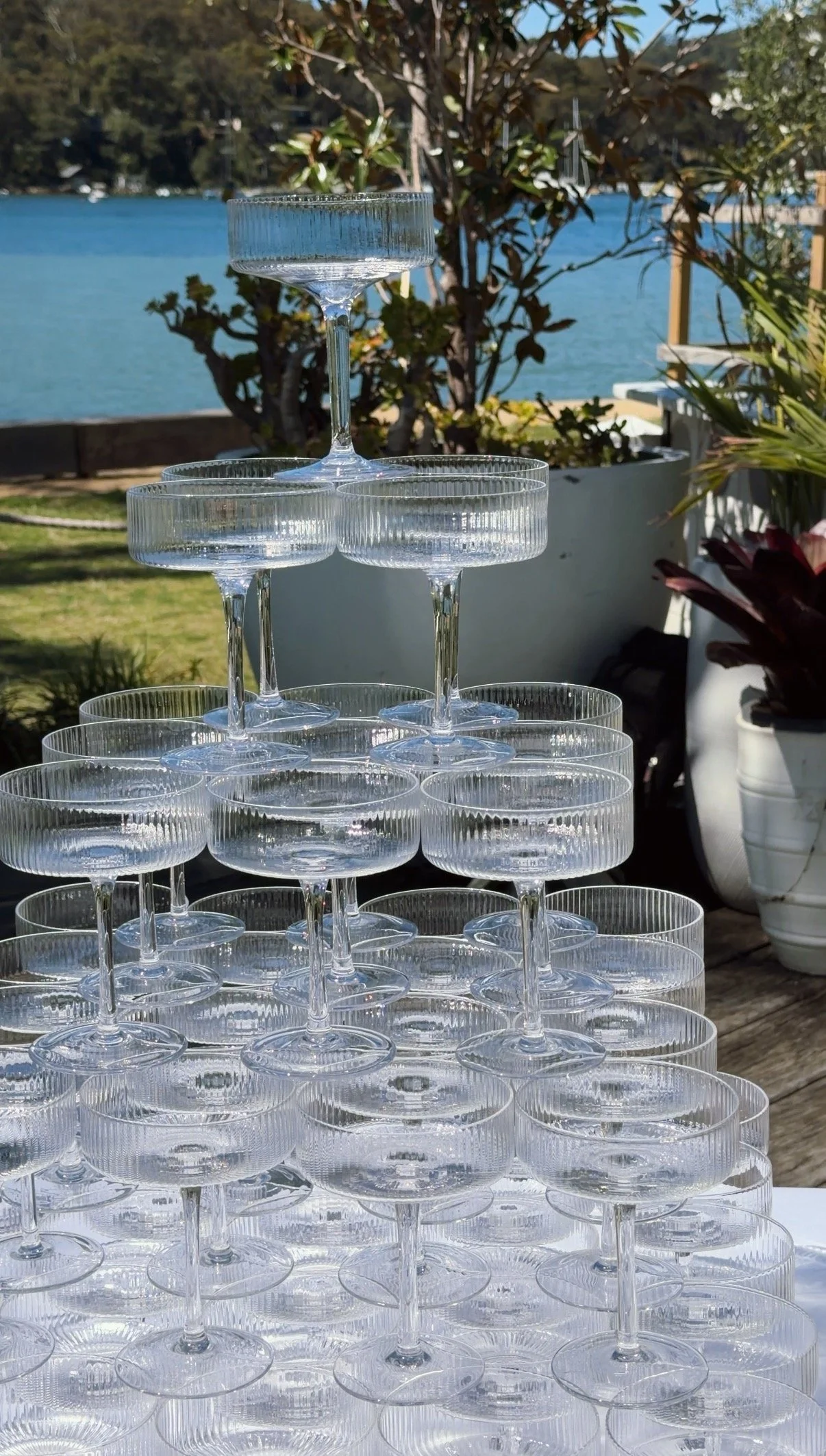Stacked Clear Glass Champagne Flutes on outdoor patio with lake and trees in the background.