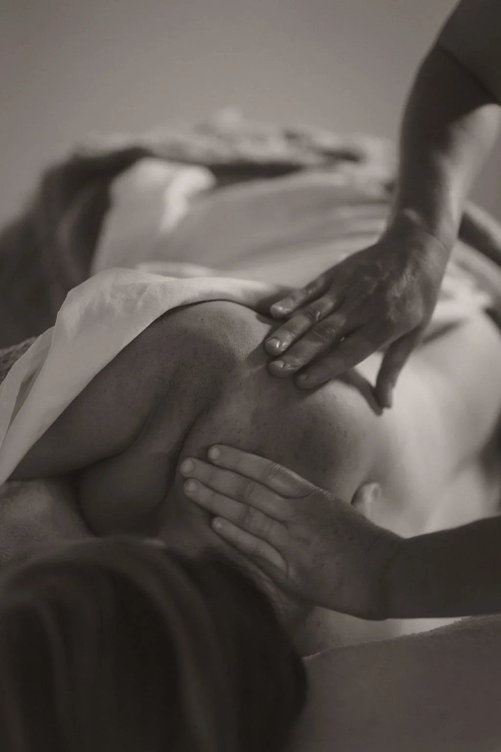 Black and white photograph of a massage therapist's hands massaging a client's back.