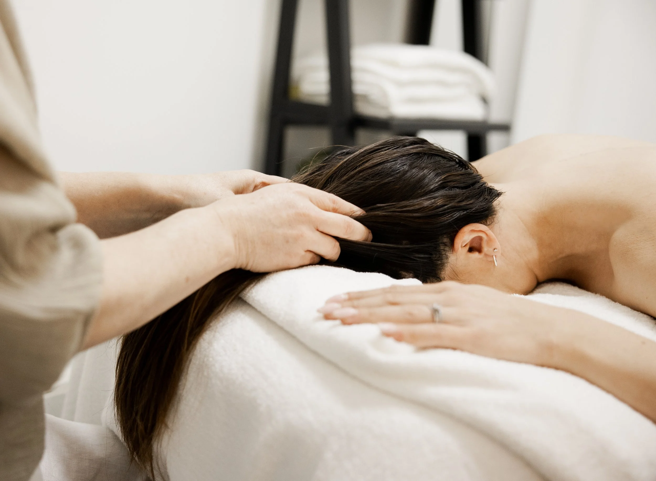 A person with dark hair receiving a massage or chiropractic adjustment on their upper back, with hands applying pressure, in a therapy or massage room.