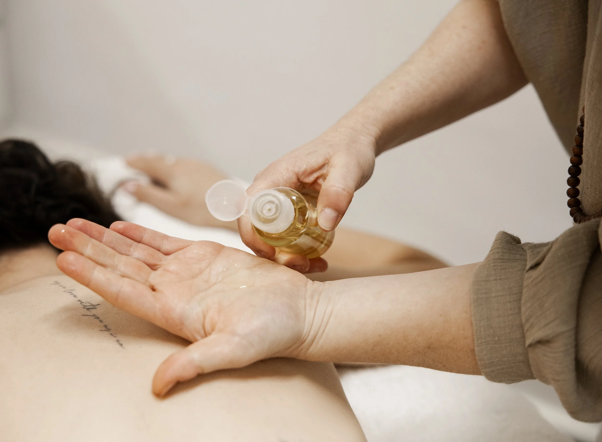 A person with a gray shirt is pouring oil from a small bottle into their palm during a massage