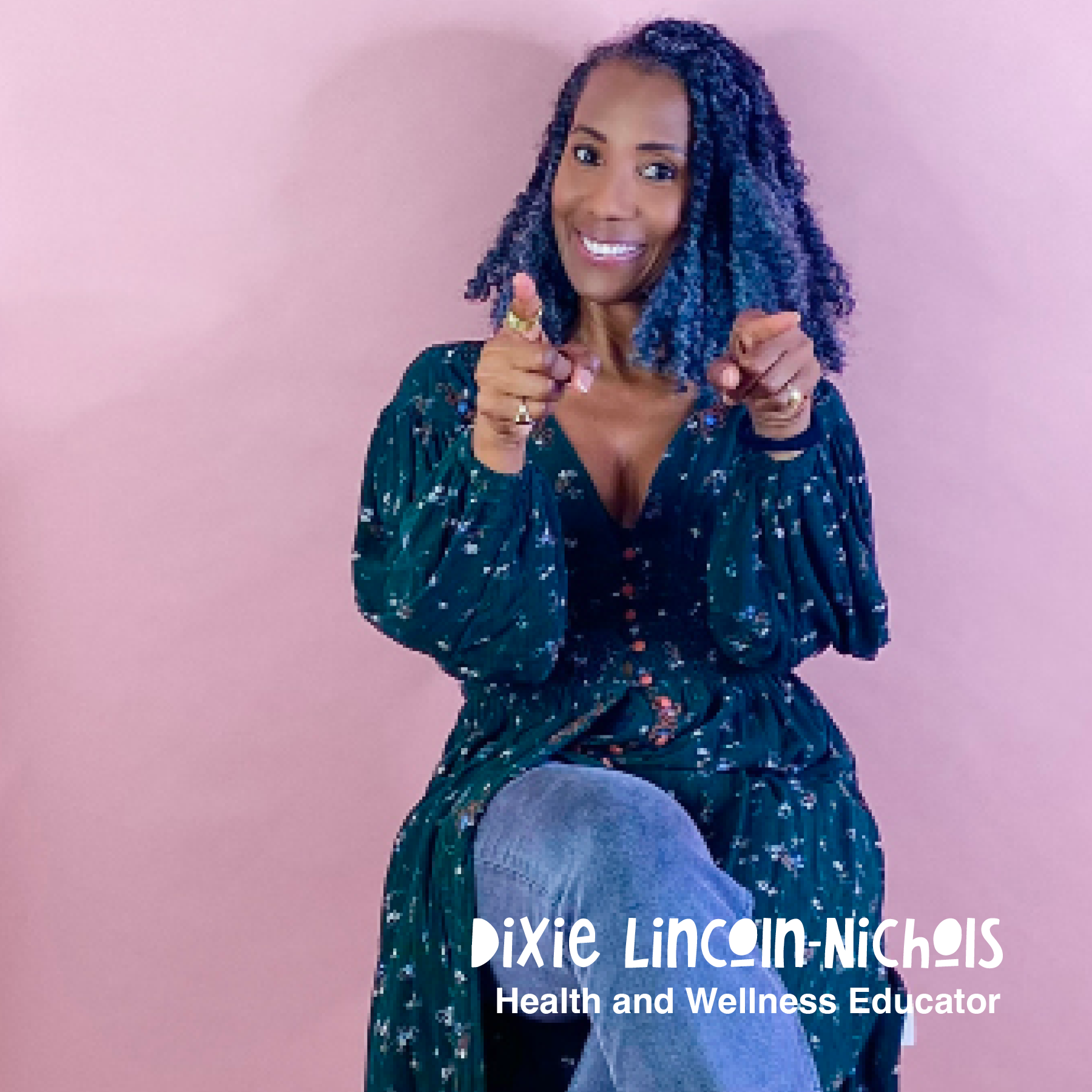 A woman sitting against a pink background smiling and pointing at the camera. She has curly, shoulder-length hair and is wearing a dark patterned dress with a deep neckline and jeans. Text on the image reads: 'Dixie Lincoln-Nichols, Health and Wellness Educator.'