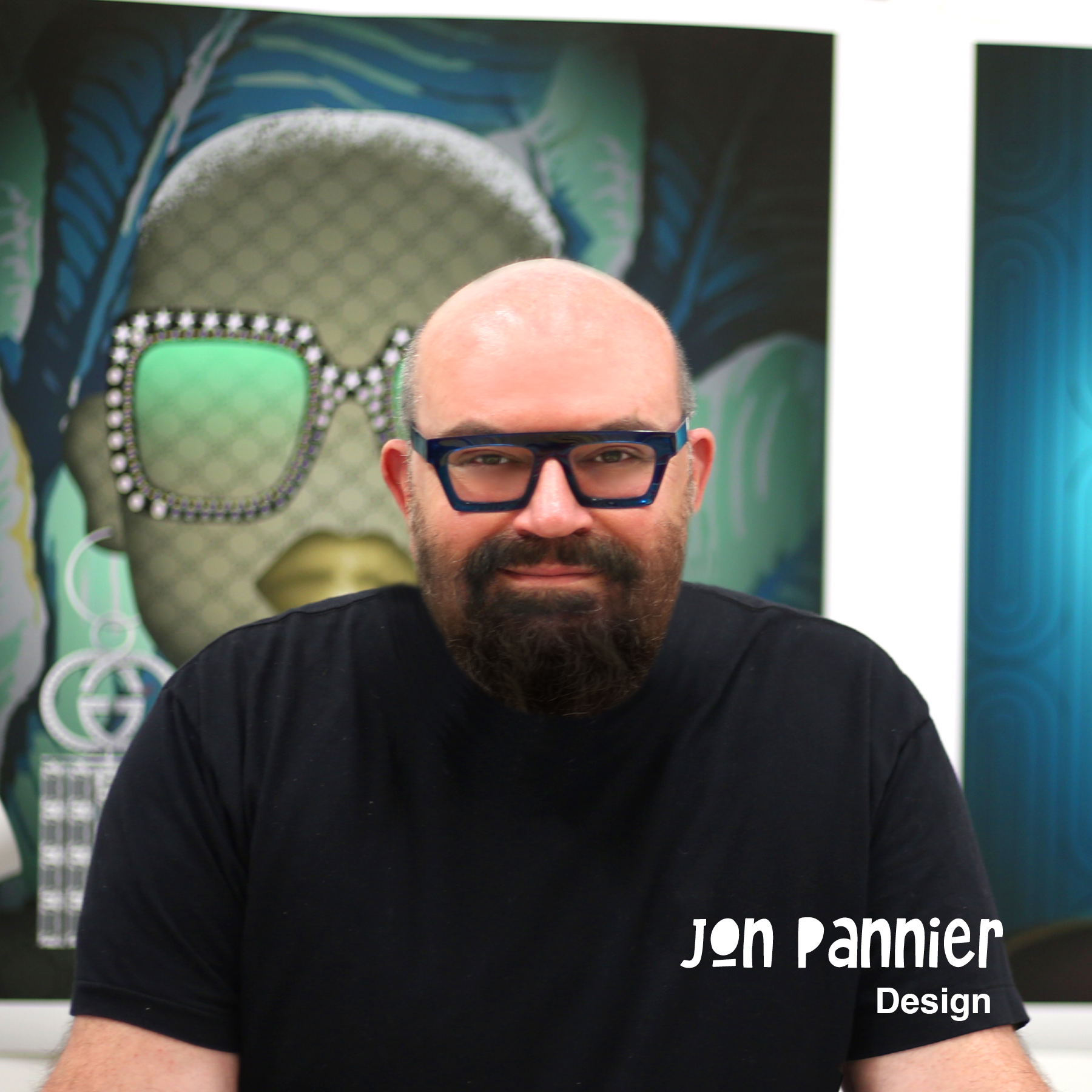 Man with a beard and glasses posing in front of pop art with a face wearing sunglasses in the background, and the text 'Jon Pannier Design' at the bottom right corner.