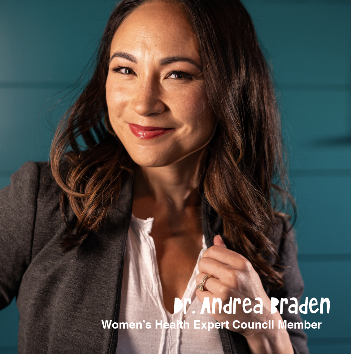 Close-up of Dr. Andrea Braden, a women’s health expert council member, smiling and looking at the camera, wearing a dark blazer and white top, standing against a teal background.