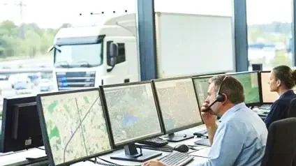 Dos personas trabajando en una sala de control con múltiples monitores, uno de ellos usando auriculares.