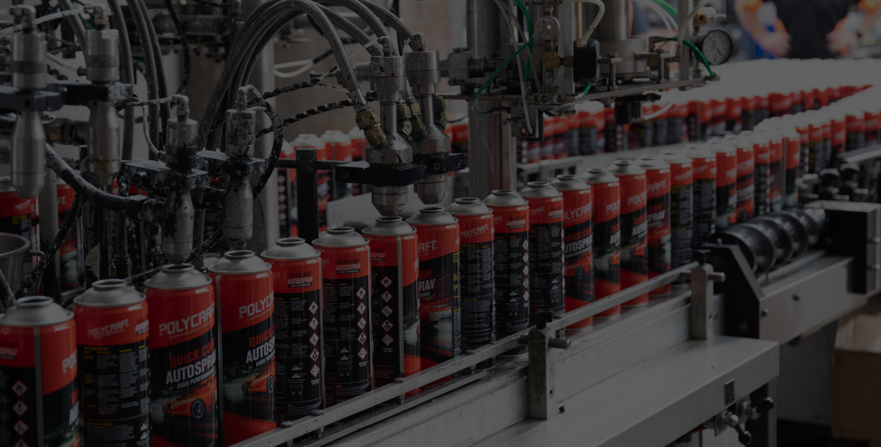 Industrial spray paint cans on a conveyor belt with machinery, in a factory setting, with a person in the background.
