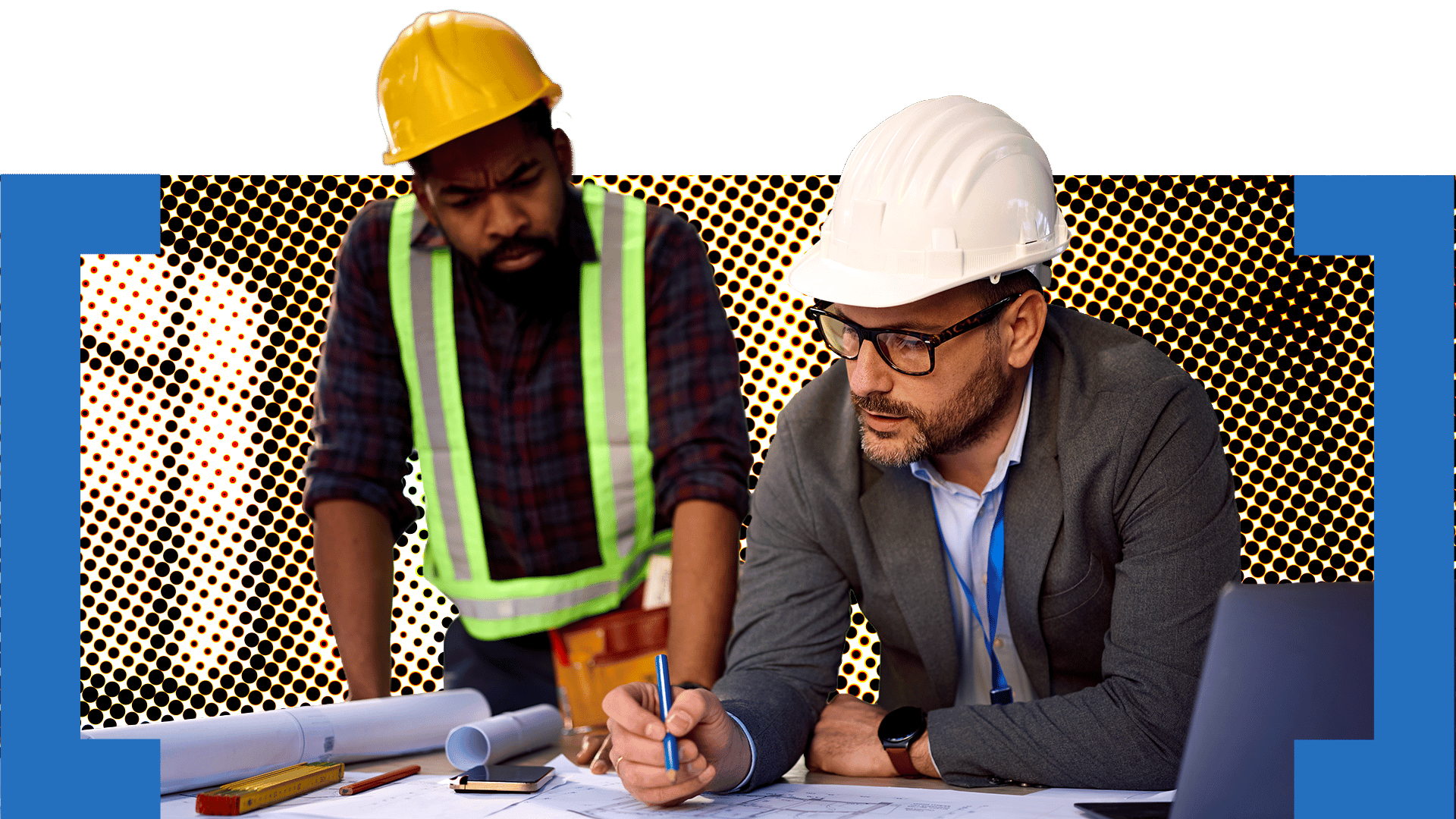 Two men wearing safety helmets and safety vests working at a desk with blueprints and a laptop.