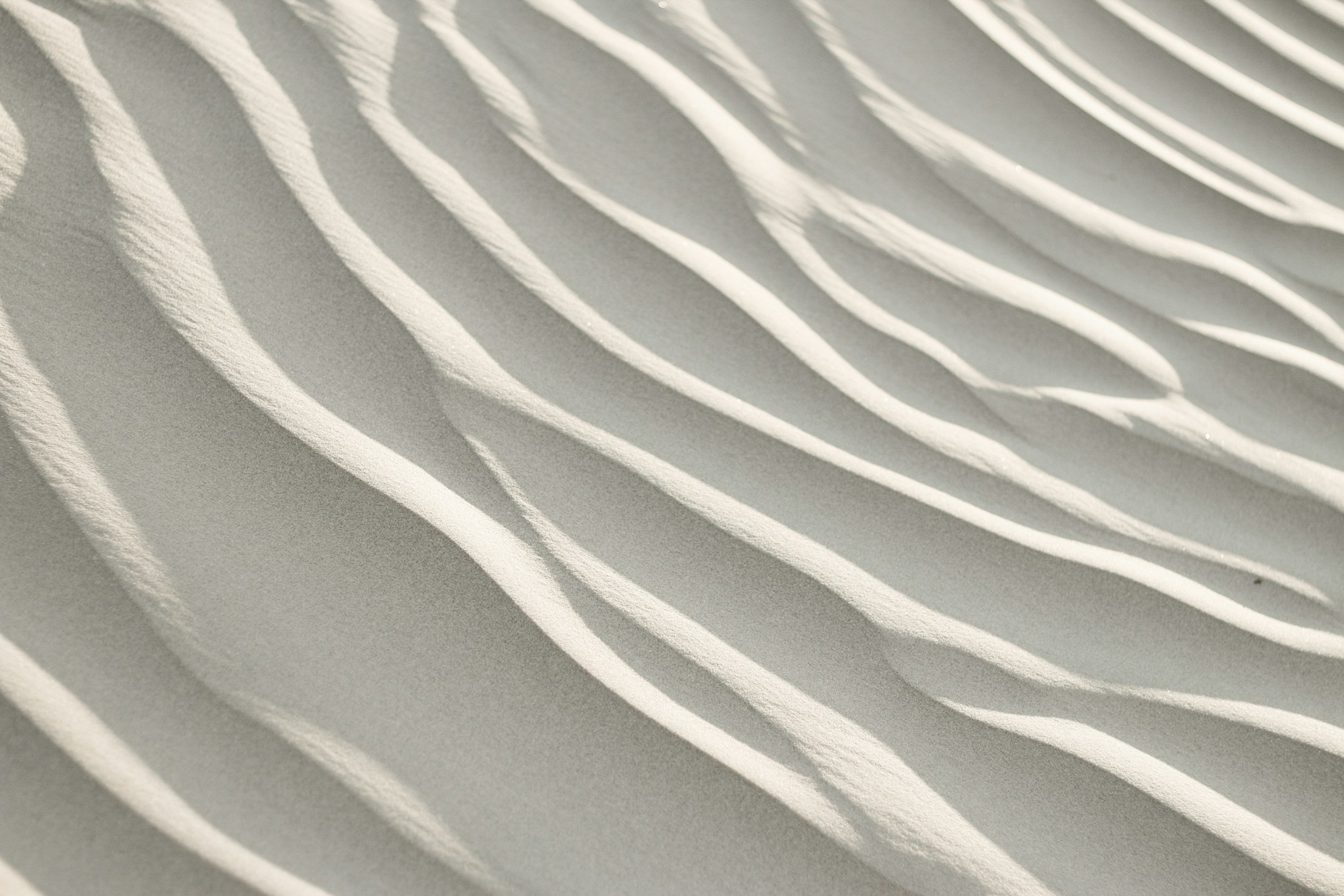 Close-up of white, curved architectural louvers casting shadows on a wall.
