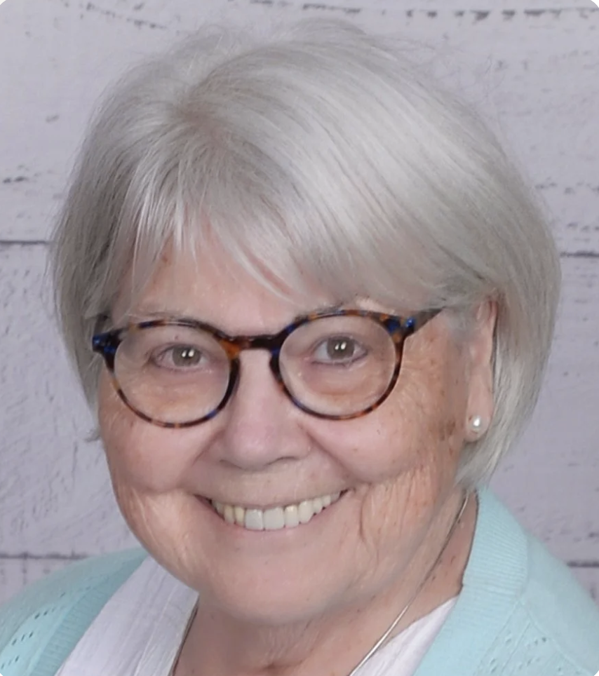 Lynn Scott, EMDR Therapist, wearing glasses, a pearl earring, and a light blue cardigan, smiling in front of a light wooden background.