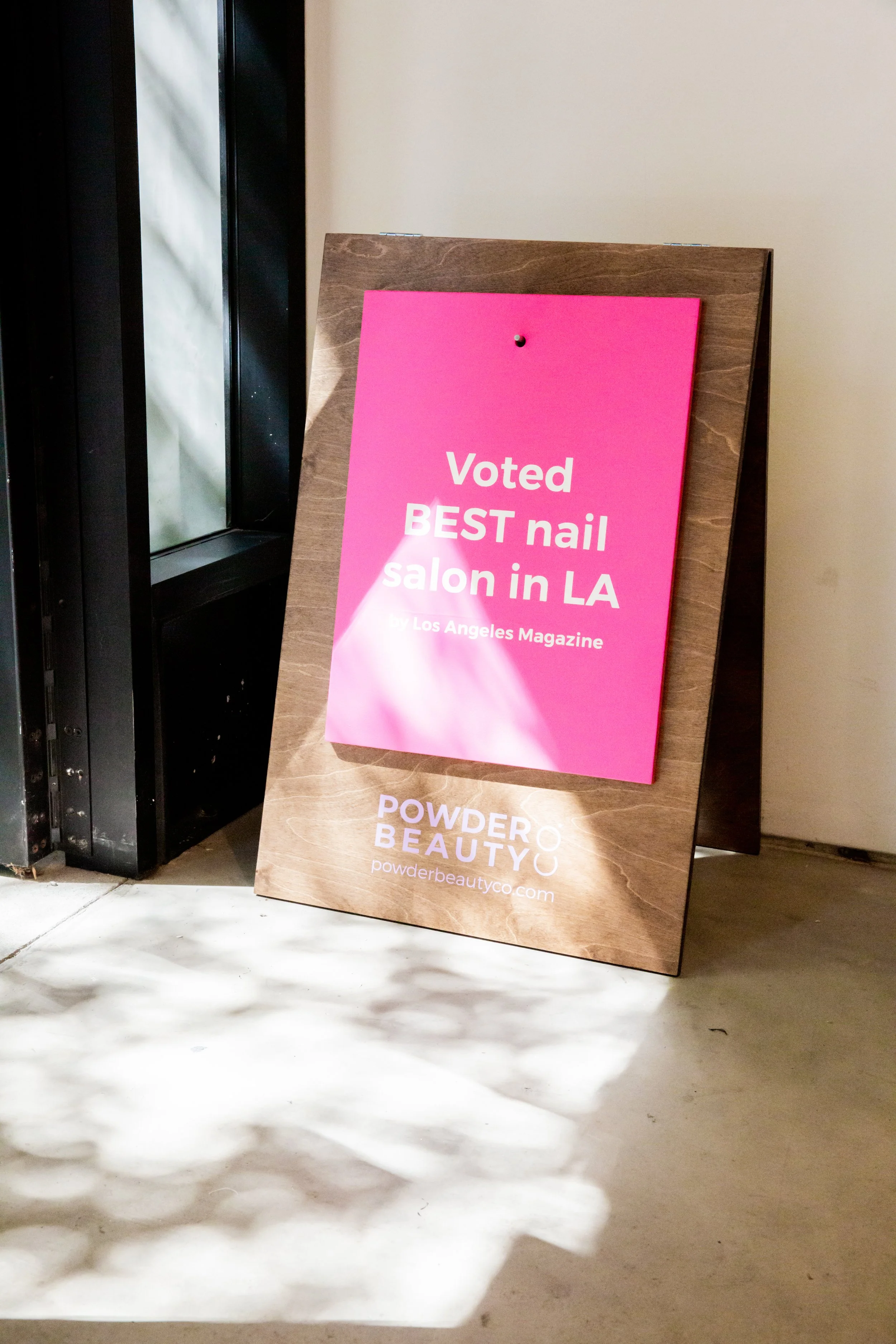 Pink signboard outside a store at Powder Beauty Co in Los Angeles, stating it was voted best nail salon in LA by Los Angeles Magazine.
