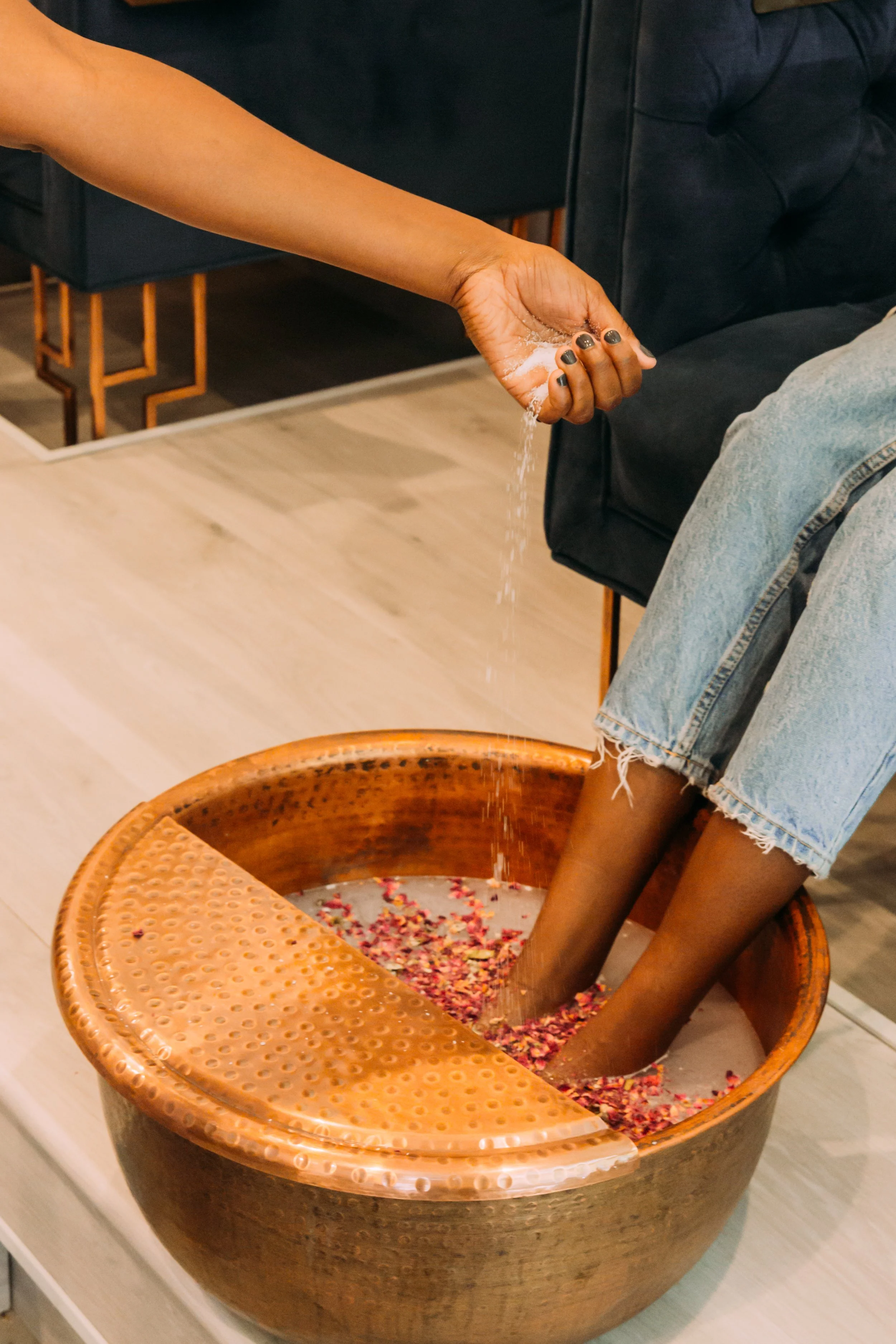 Person pouring flower petals into a large, round, brown decorative bowl on a light-colored floor for a pedicure in DTLA
