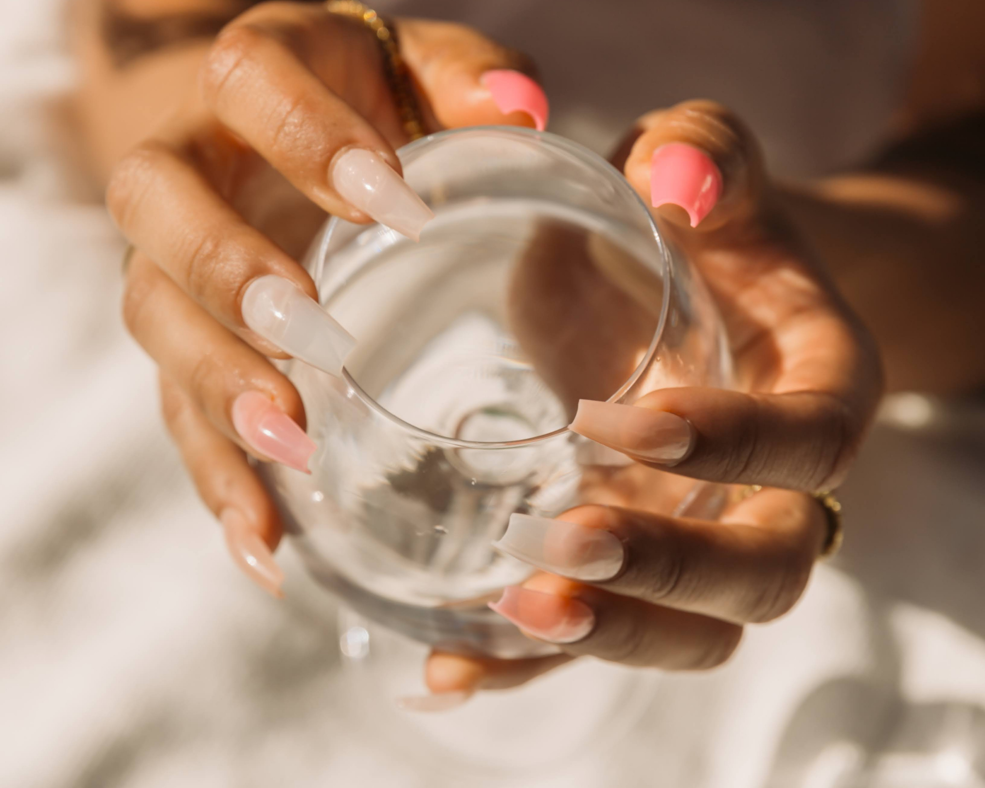 Close-up of a person's hand with long acrylic nails holding a clear glass of water.