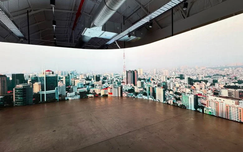 View of a cityscape from a high vantage point inside a building with panoramic curved screens showing the city skyline during daytime.