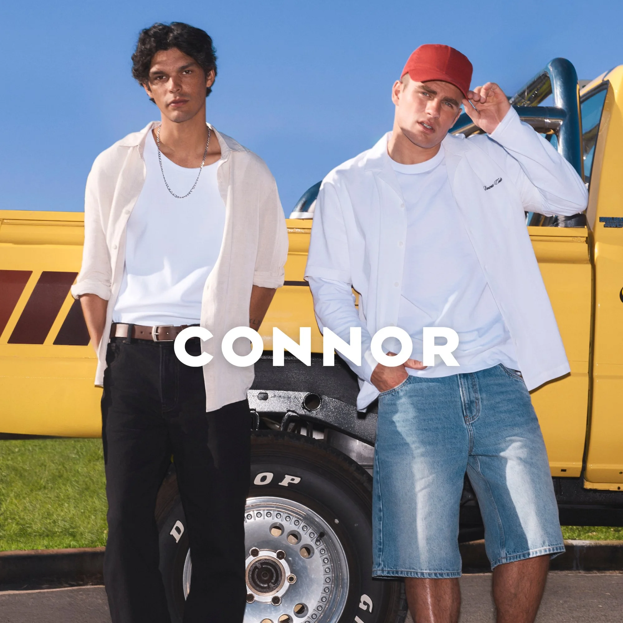 Two young men standing in front of a yellow vehicle with large tires, one wearing a white shirt and red cap, the other with dark hair and a white shirt, against a clear blue sky. The word 'CONNOR' is written across the image.