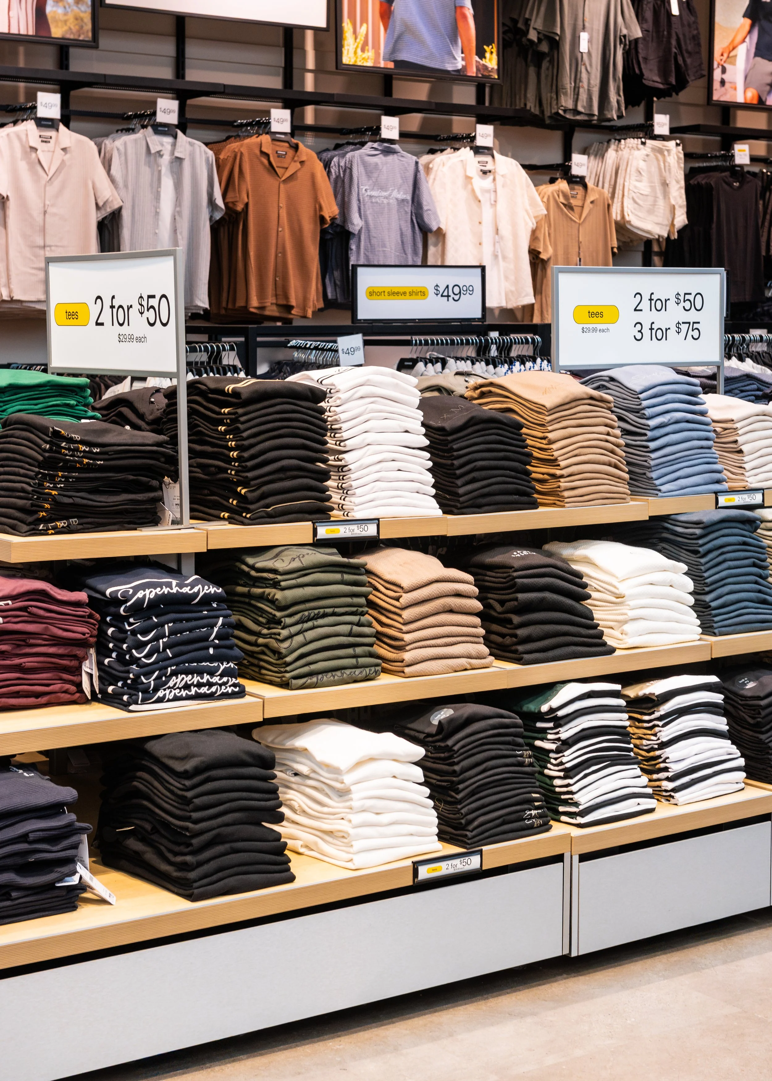 Clothing store display with neatly folded shirts and signage for discounts on tees and short sleeve shirts.