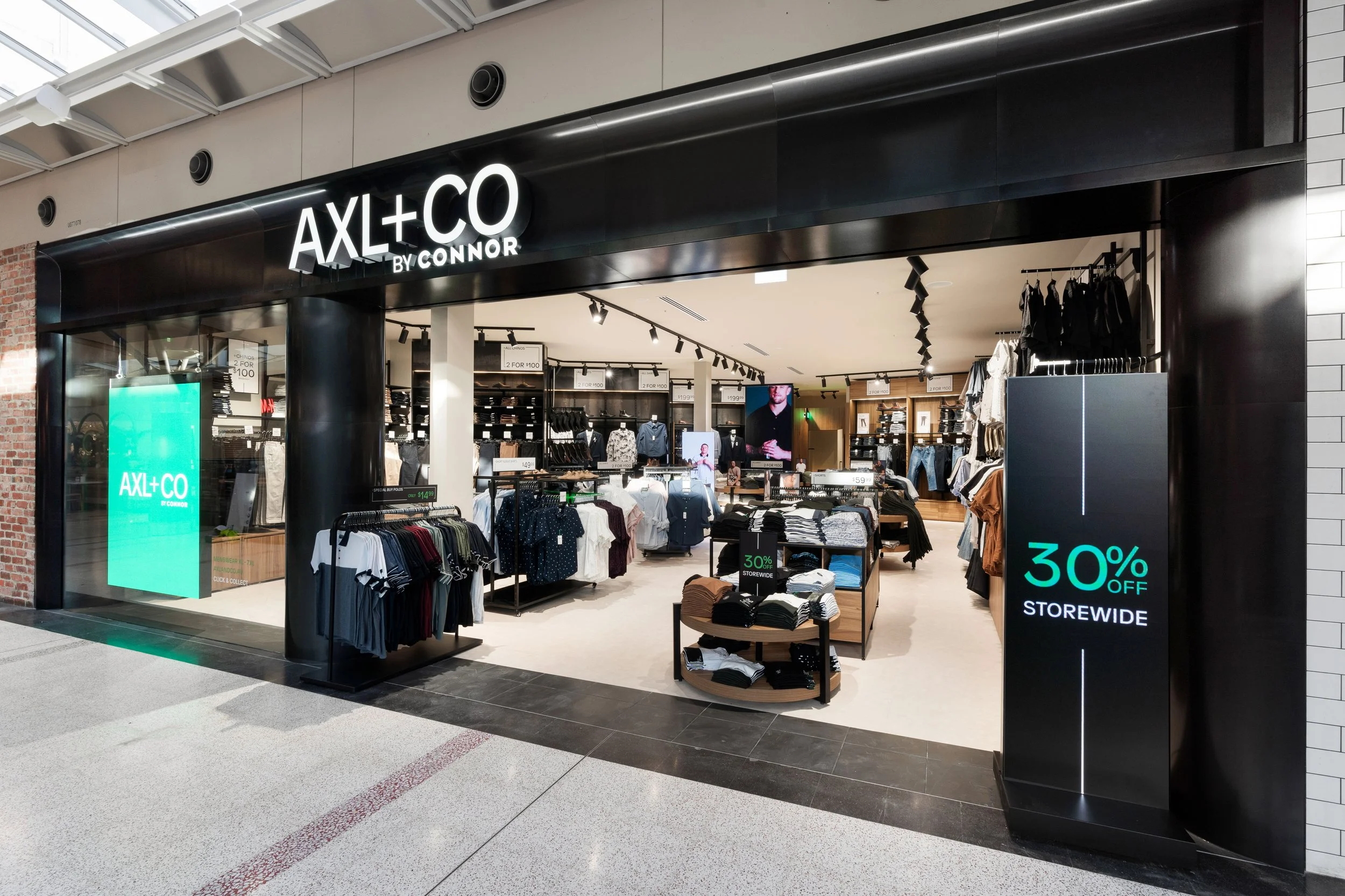 Clothing store named AX+CO by Connor inside a mall, featuring shirts, pants, and accessories on display with promotional signs offering 30% off storewide.