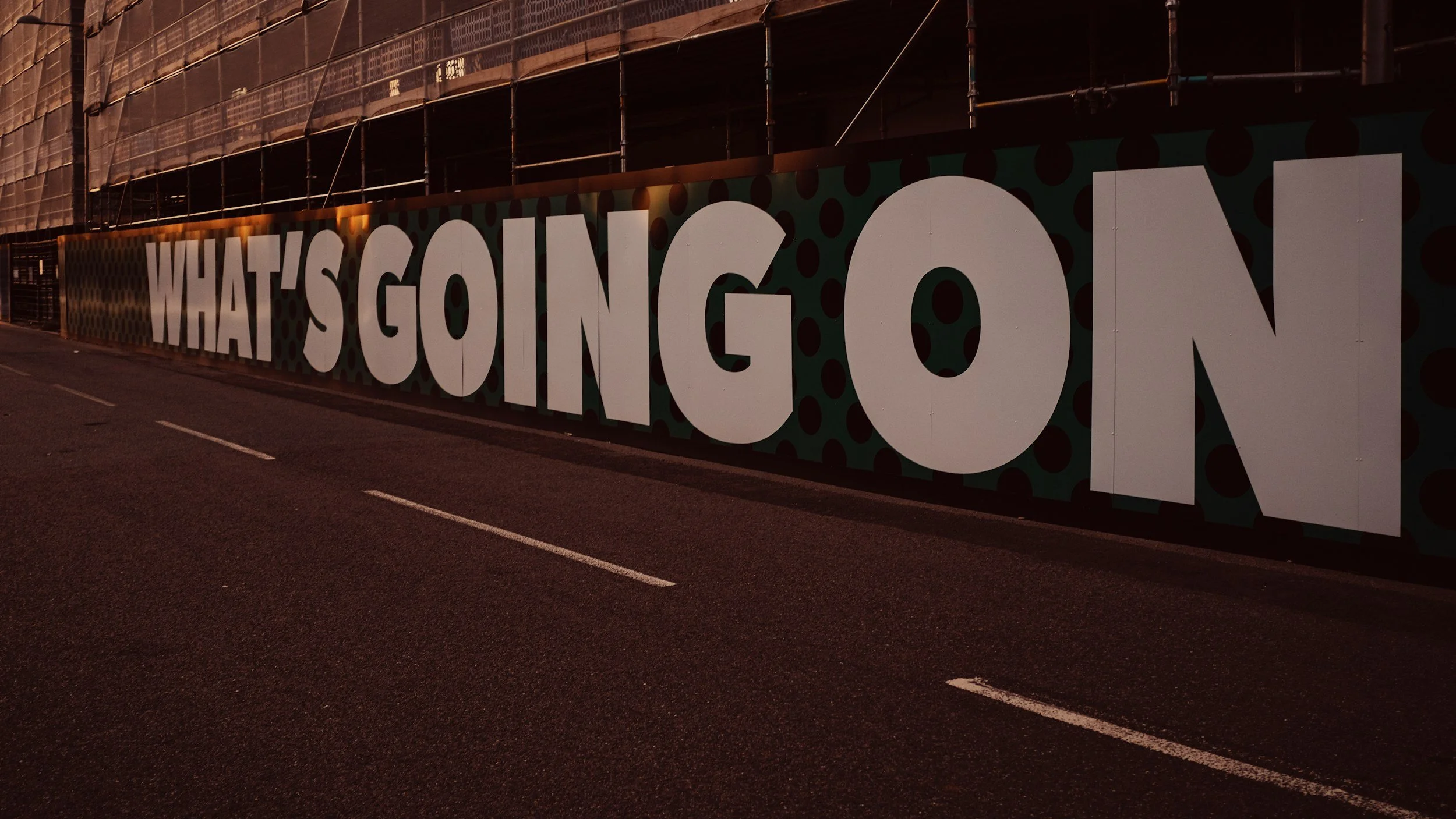 Large white letters spelling 'WHAT'S GOING ON' on a mural along a city street at night.