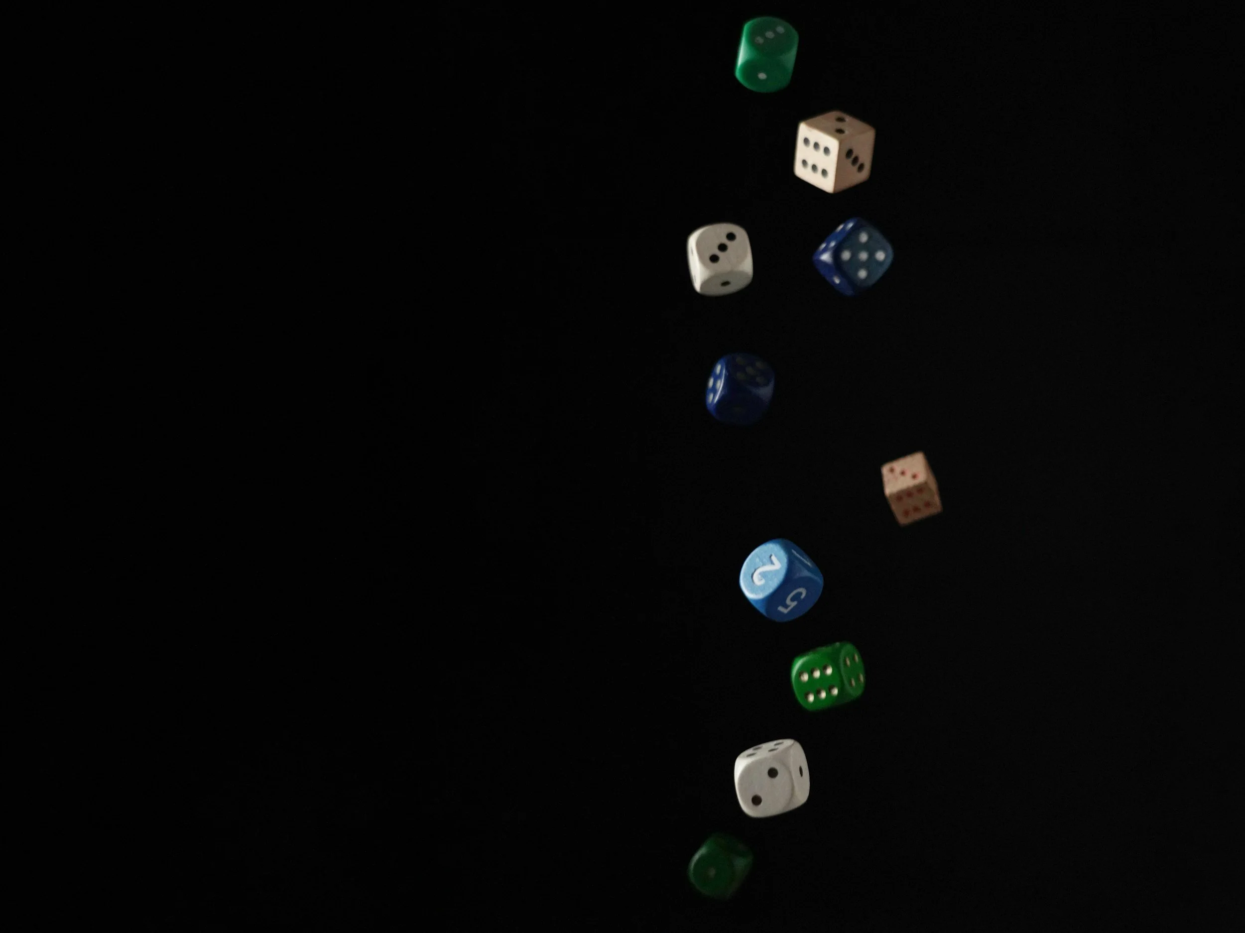 A collection of six dice in various colors (green, white, blue) is shown mid-air against a black background, with some showing the number five and others showing the number three.