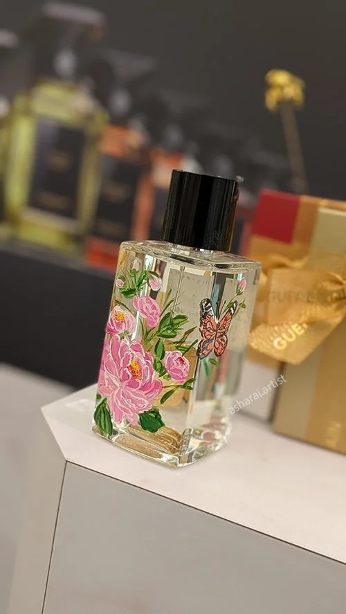 Live bottle painting by an event artist, featuring hand-painted pink peonies and a butterfly on a Chanel Coromandel Scented Body Oil bottle at Holt Renfrew, Square One, Mississauga.