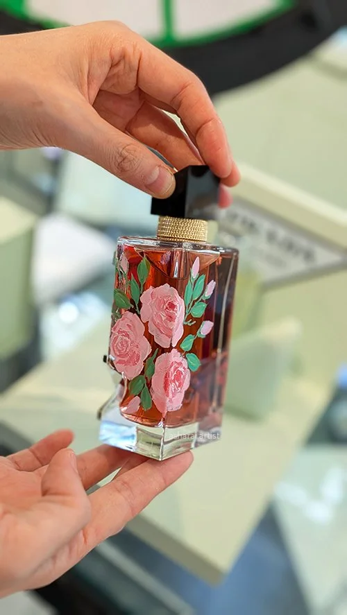 Person holding a rectangular glass perfume bottle with pink rose floral design and black cap.
